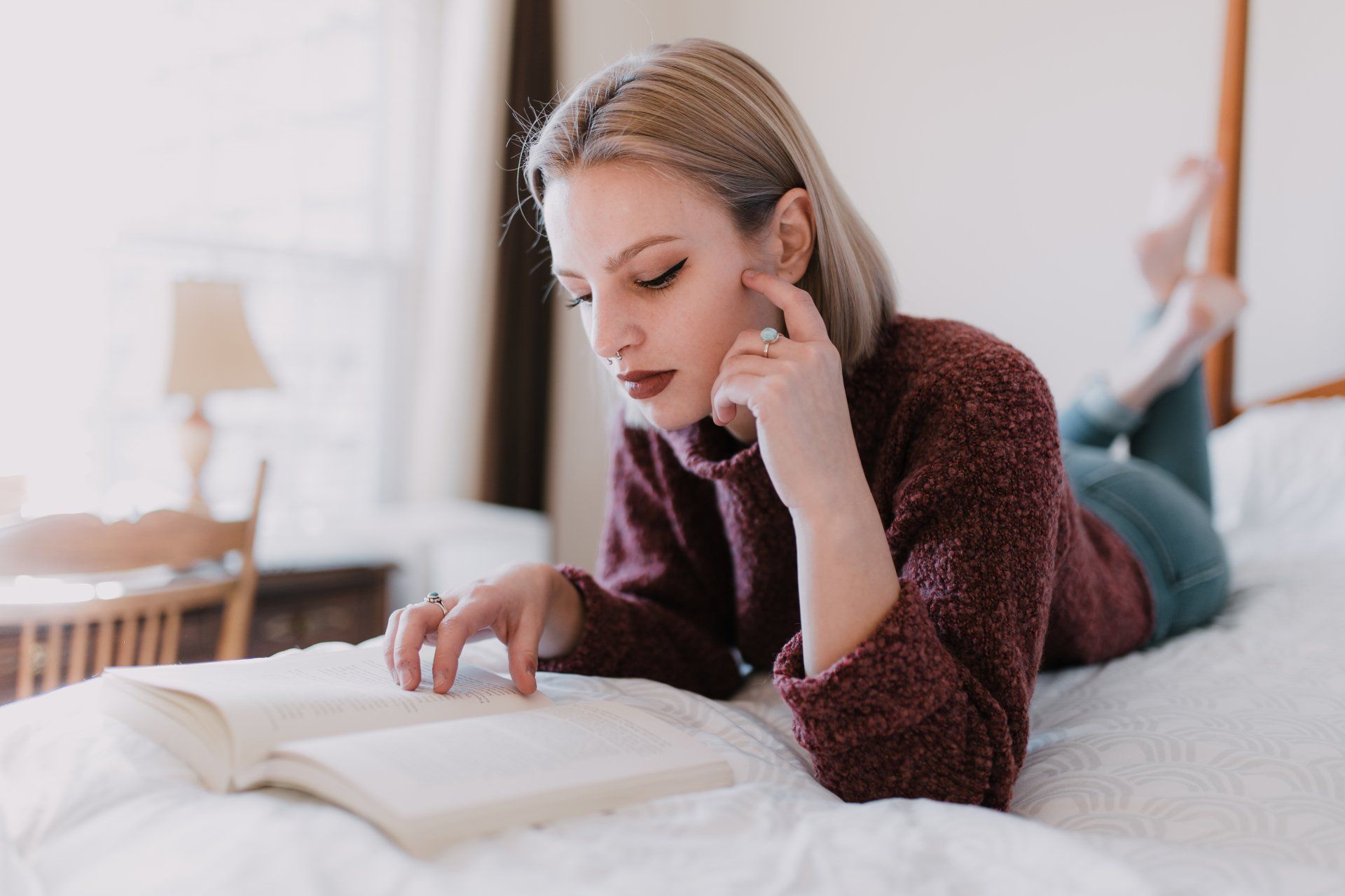A woman is laying on her stomach on a bed reading a book.