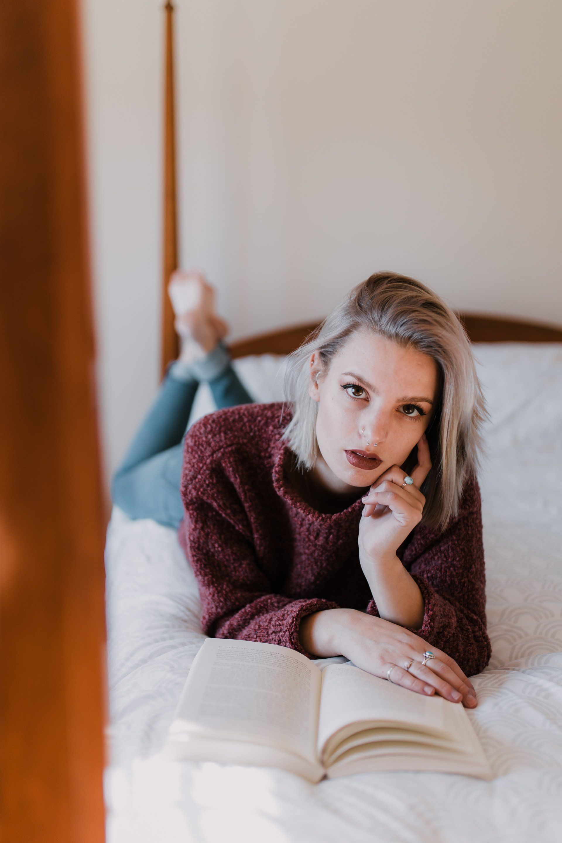 A woman is laying on her stomach on a bed reading a book.