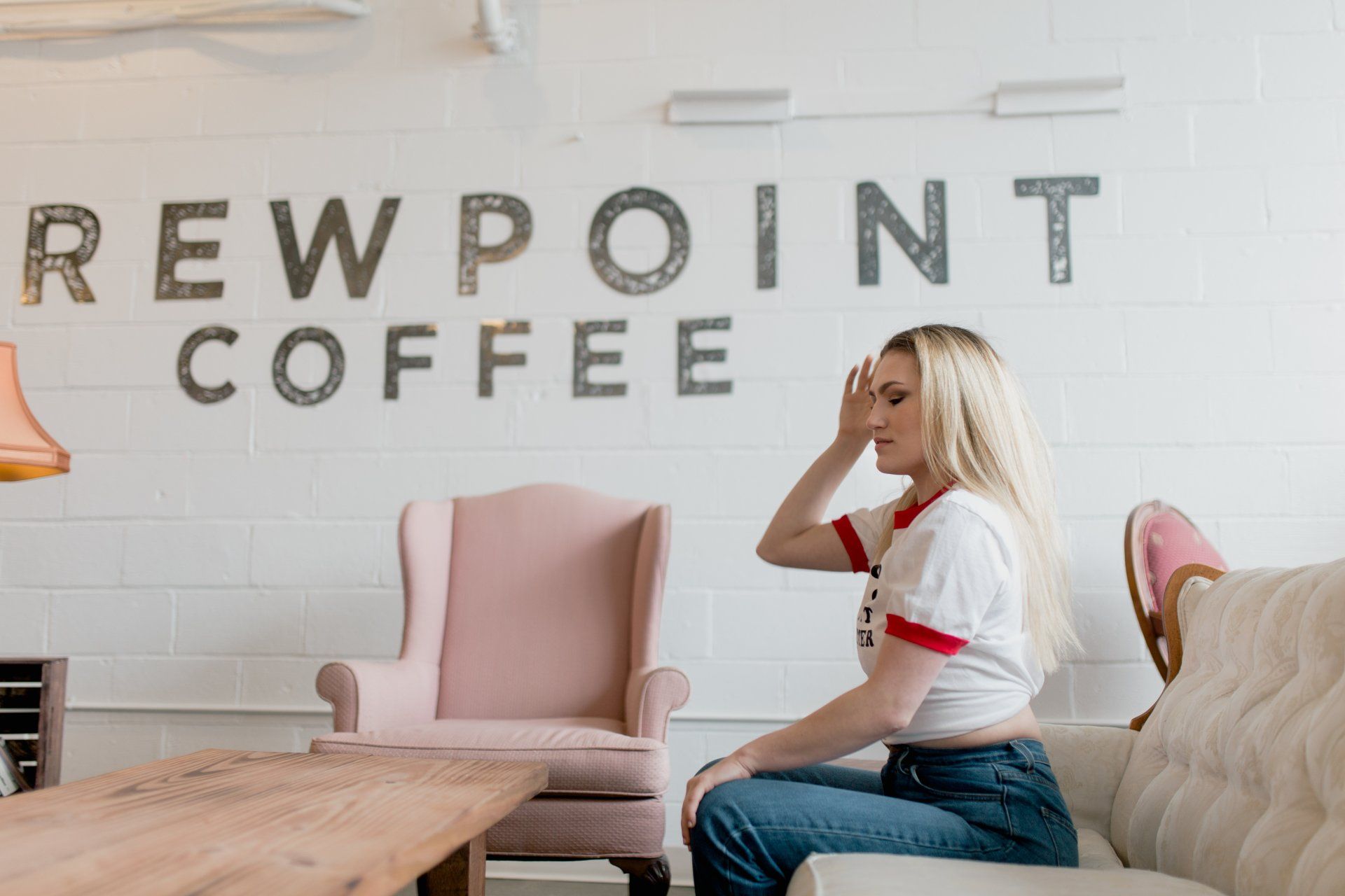 A woman is sitting on a couch in front of a sign that says brewpoint coffee.