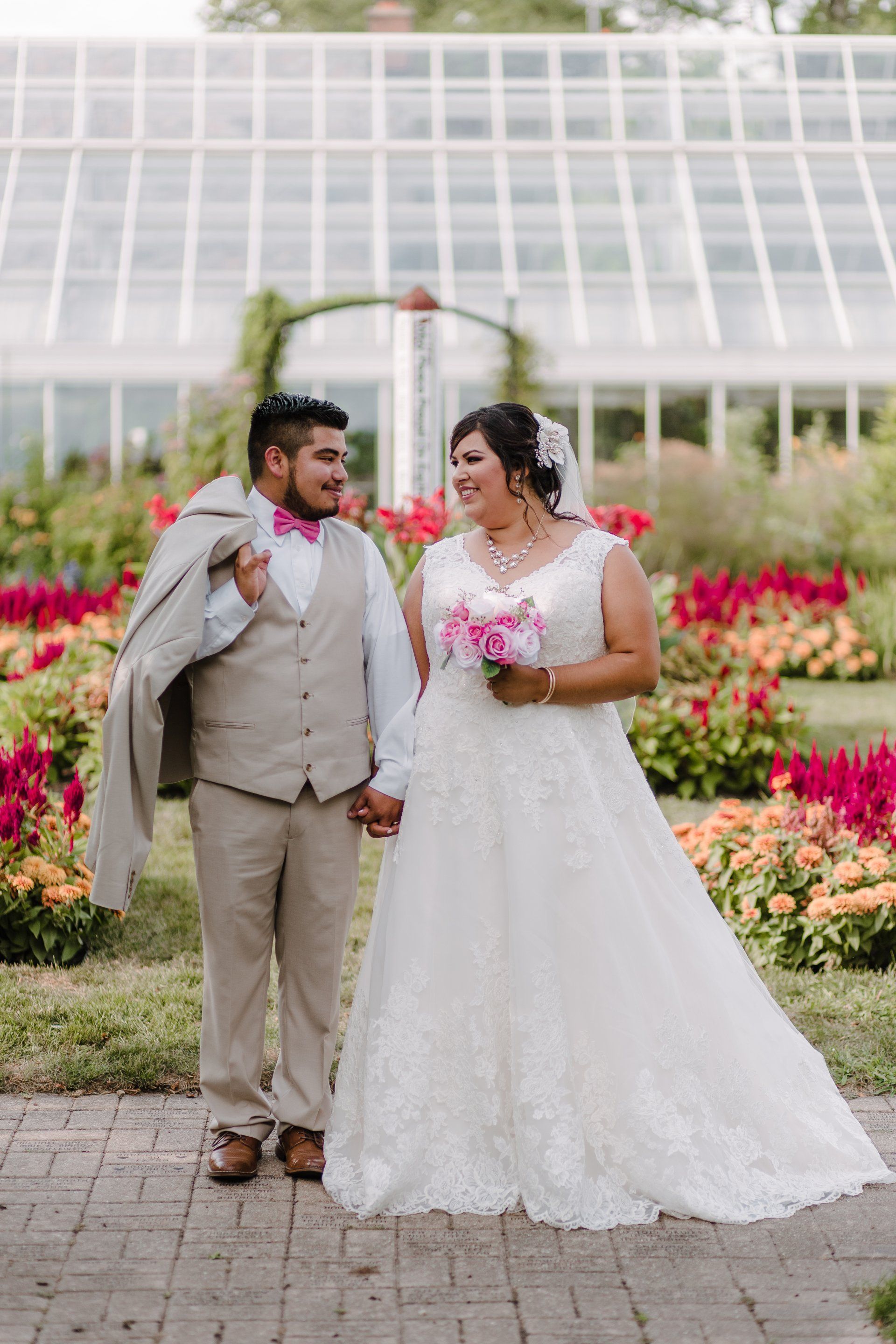 A bride and groom are holding hands in front of a greenhouse.