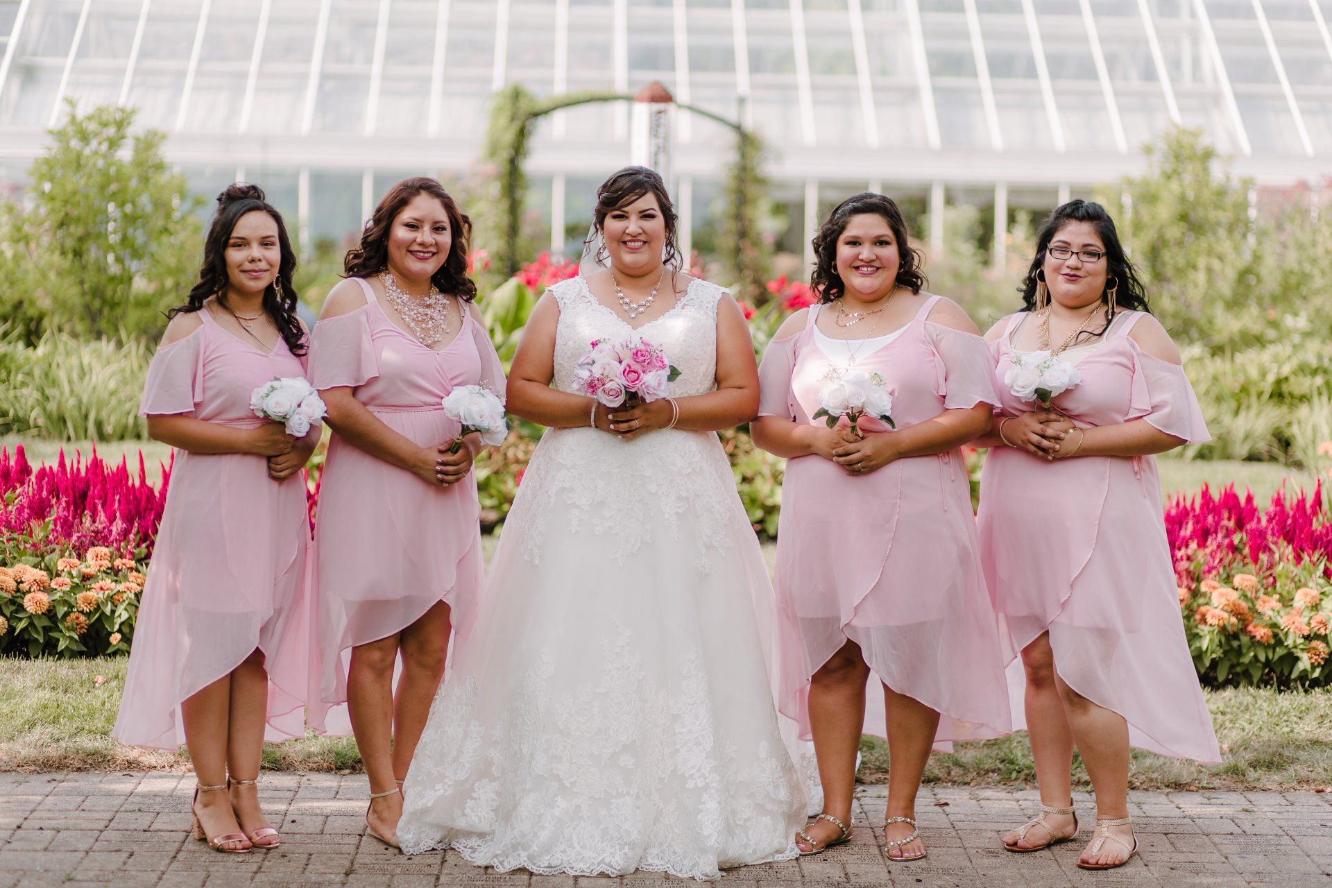 A bride and her bridesmaids are posing for a picture in front of a greenhouse.