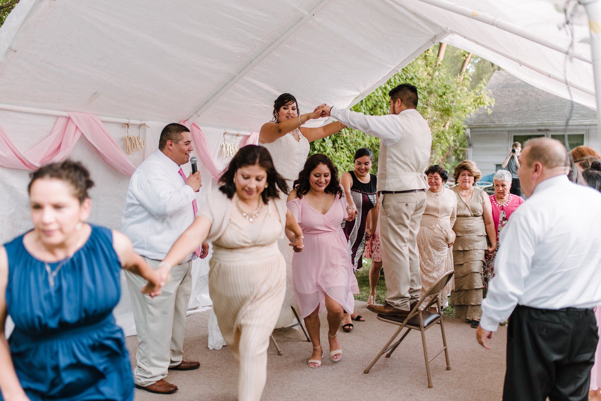 A group of people are dancing under a tent at a wedding reception.