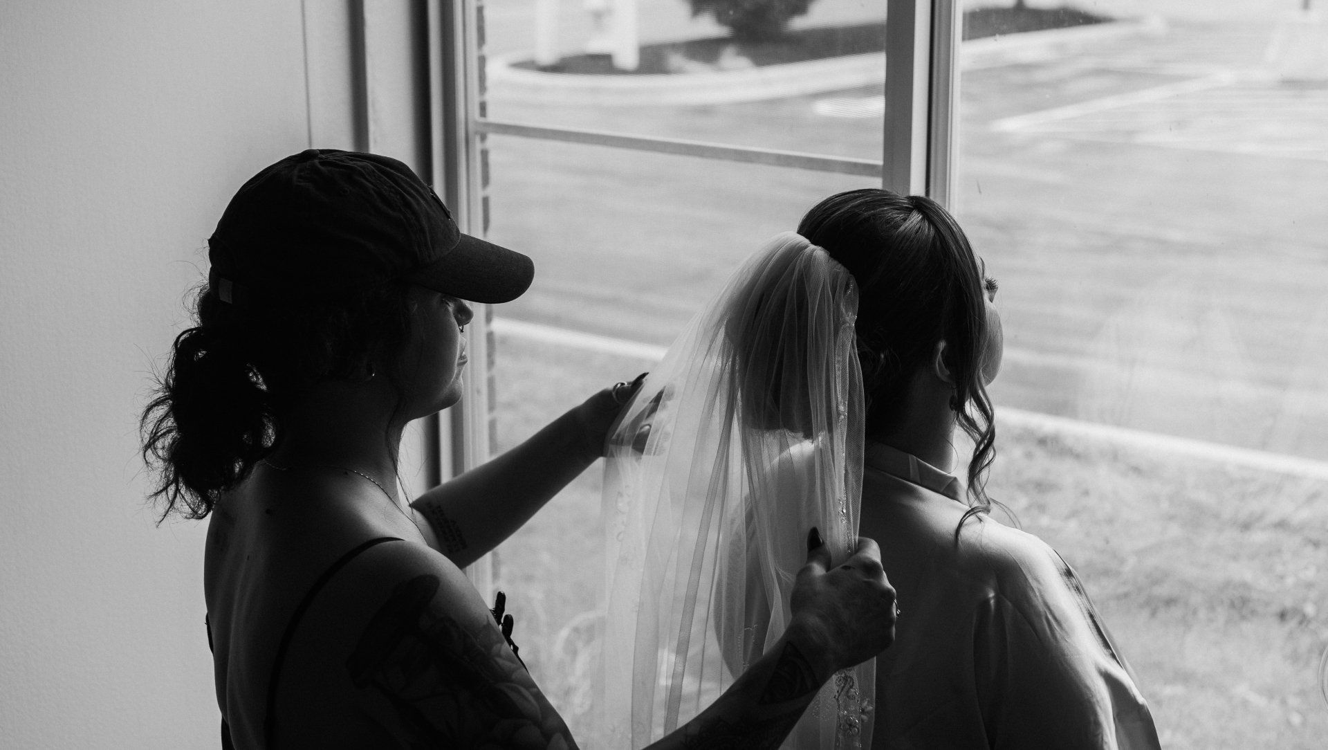 A black and white photo of a woman putting a veil on a bride.