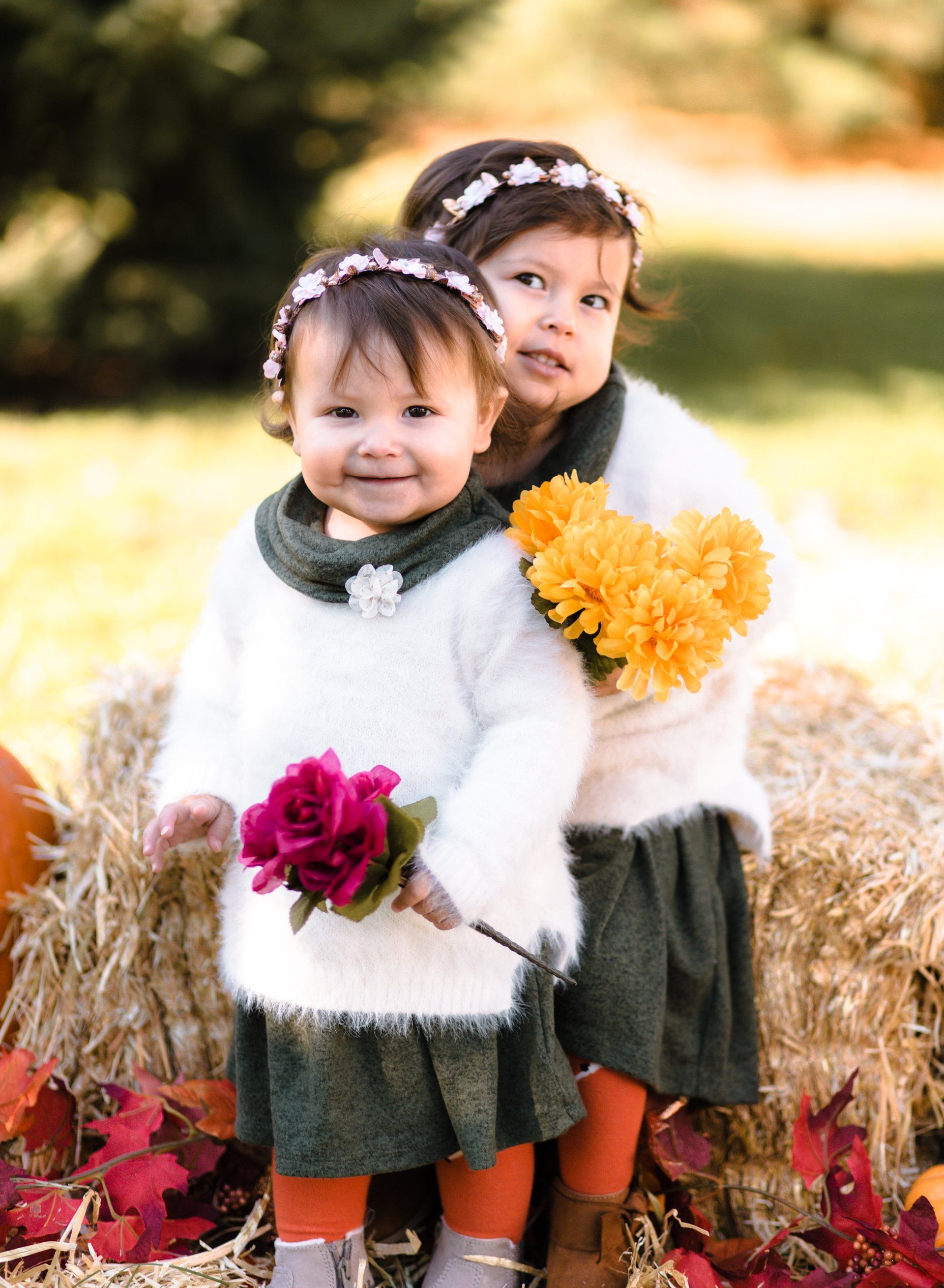 Two little girls are standing next to each other holding flowers.