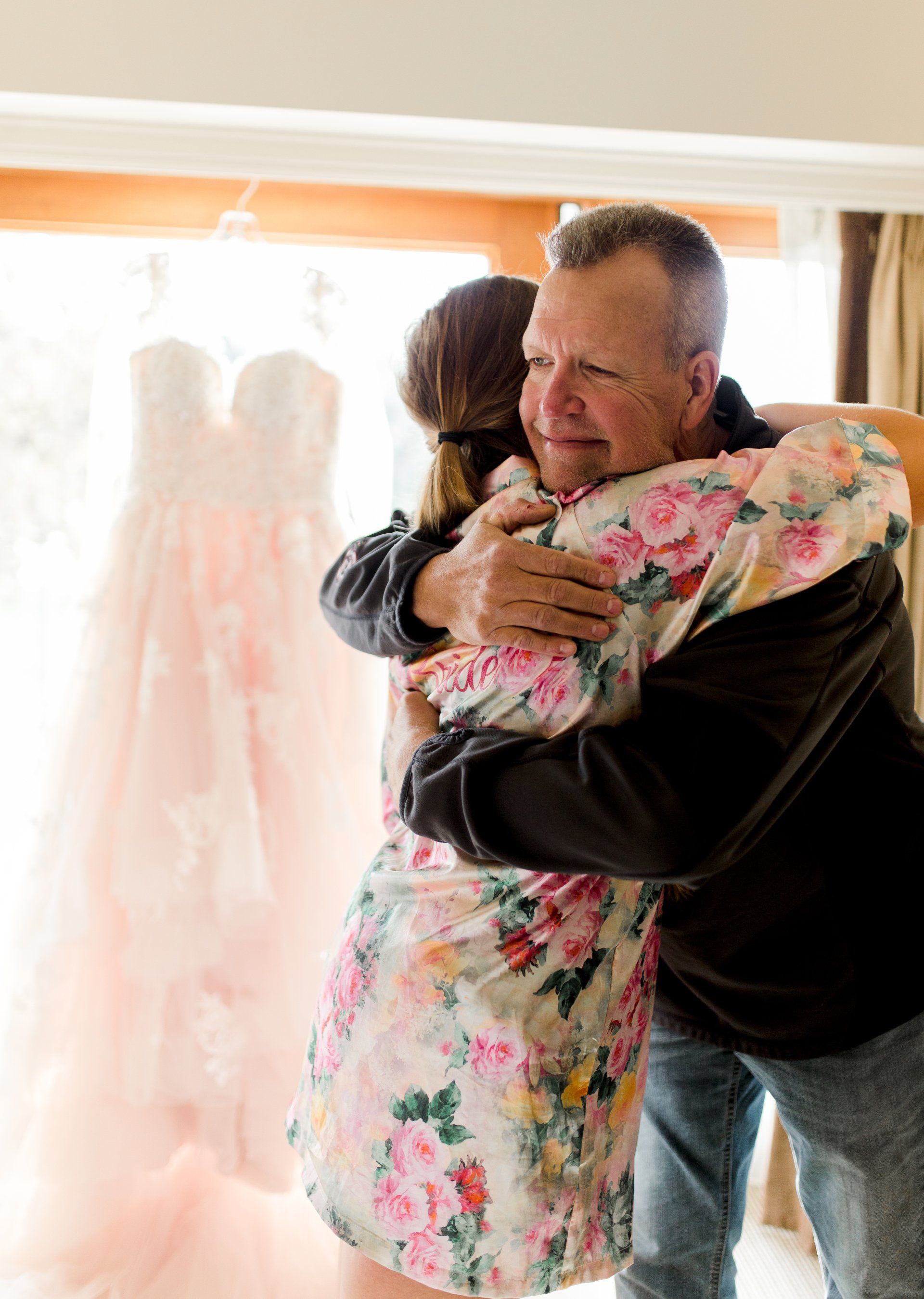 A man is hugging a woman in a floral robe in front of a window.