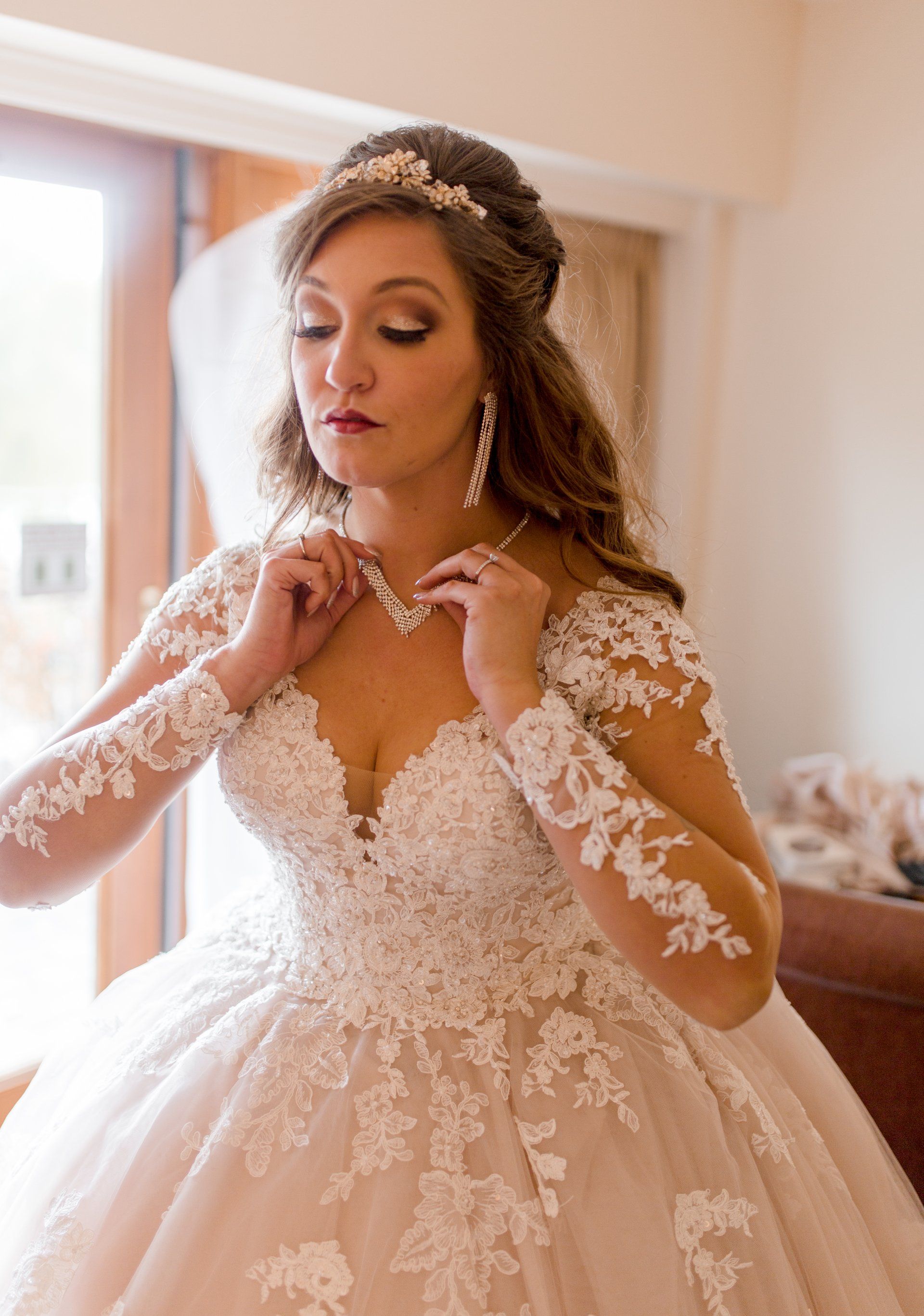 A woman in a wedding dress is putting on a necklace.