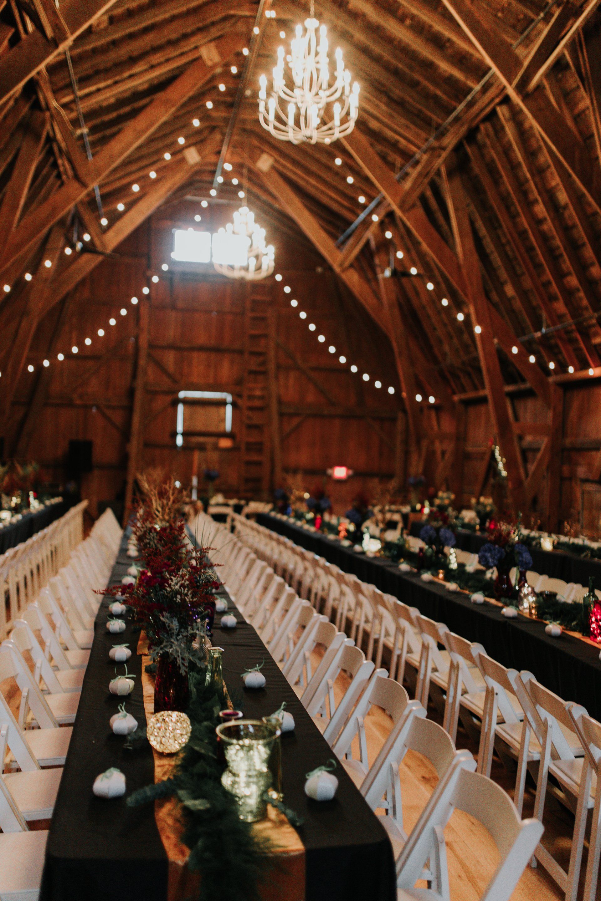 A long table in a barn is set up for a wedding reception.