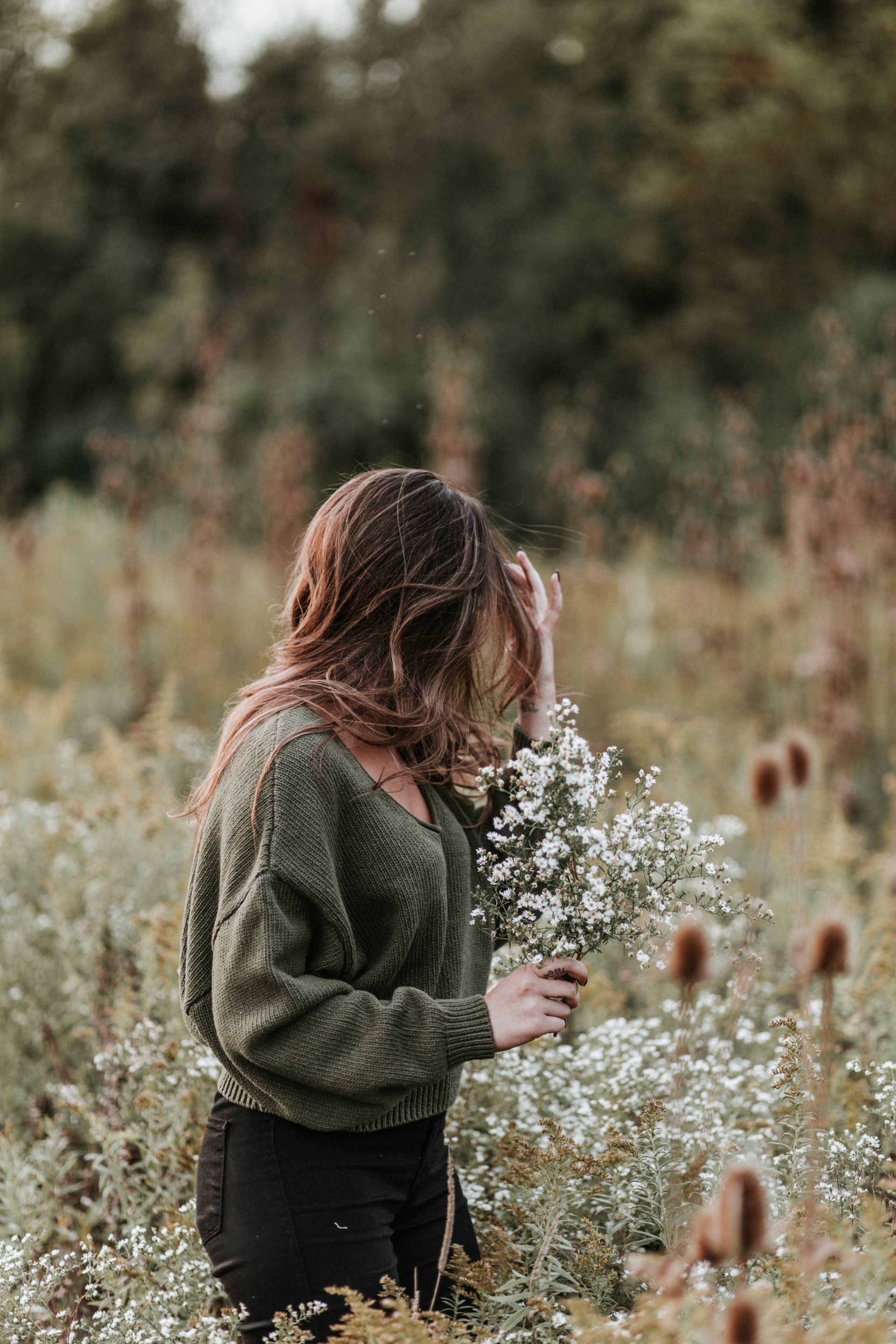 A woman in a green sweater is holding a bouquet of white flowers in a field.