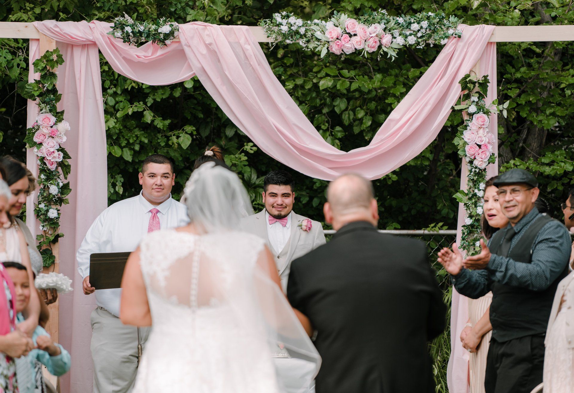 A bride and groom are getting married under a pink arch.