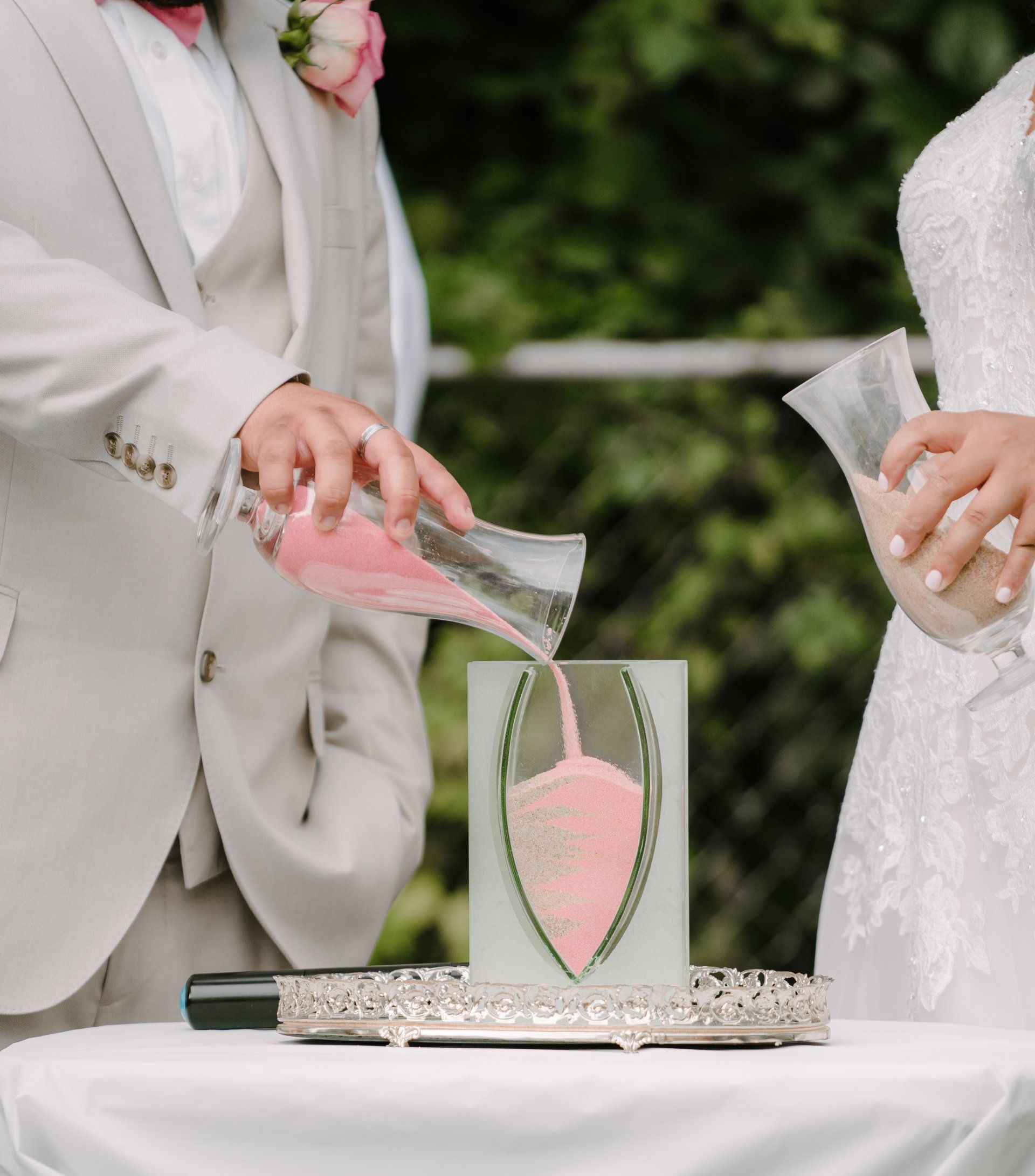 A bride and groom are pouring pink sand into a heart shaped vase