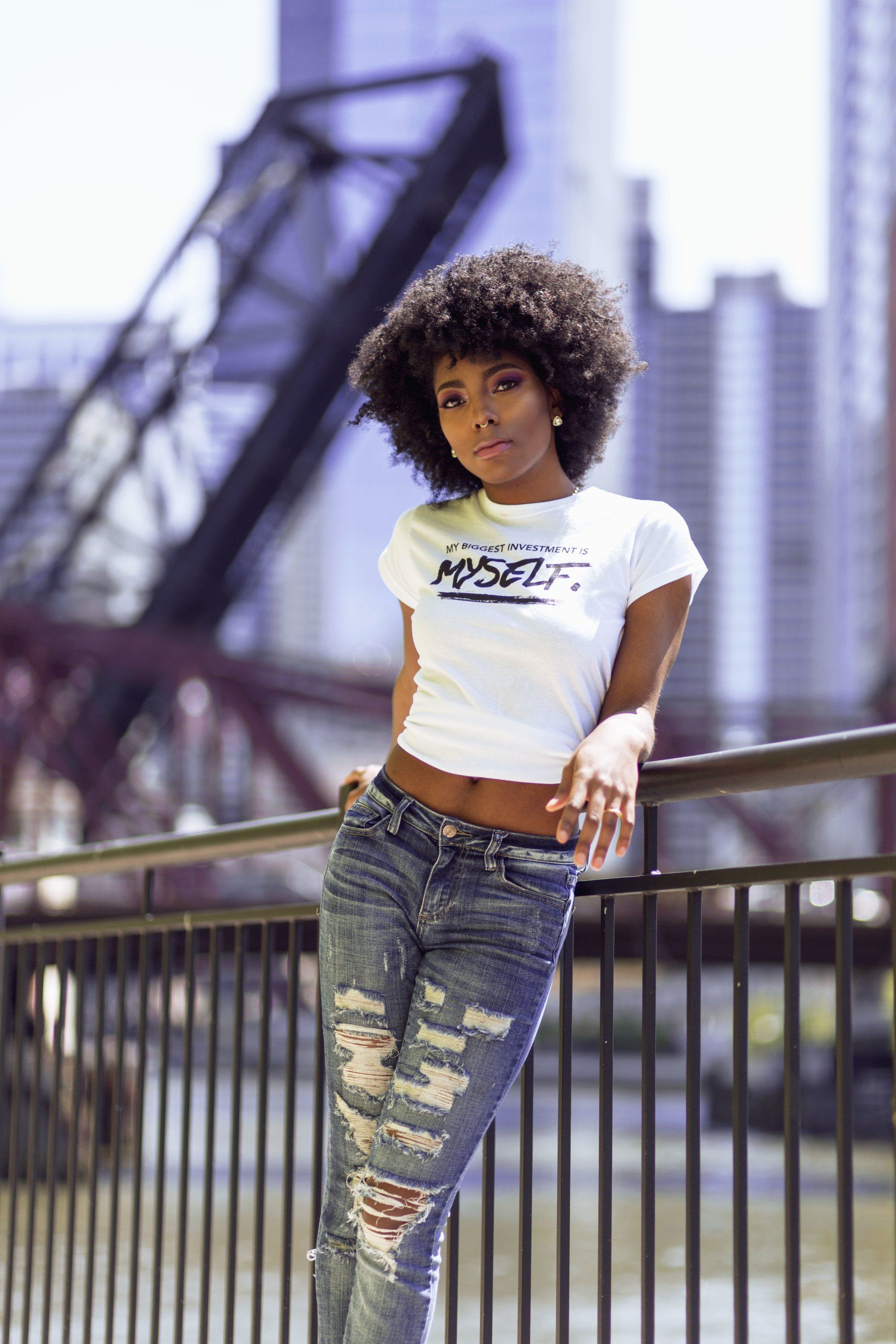 A woman is leaning on a railing in front of a bridge.