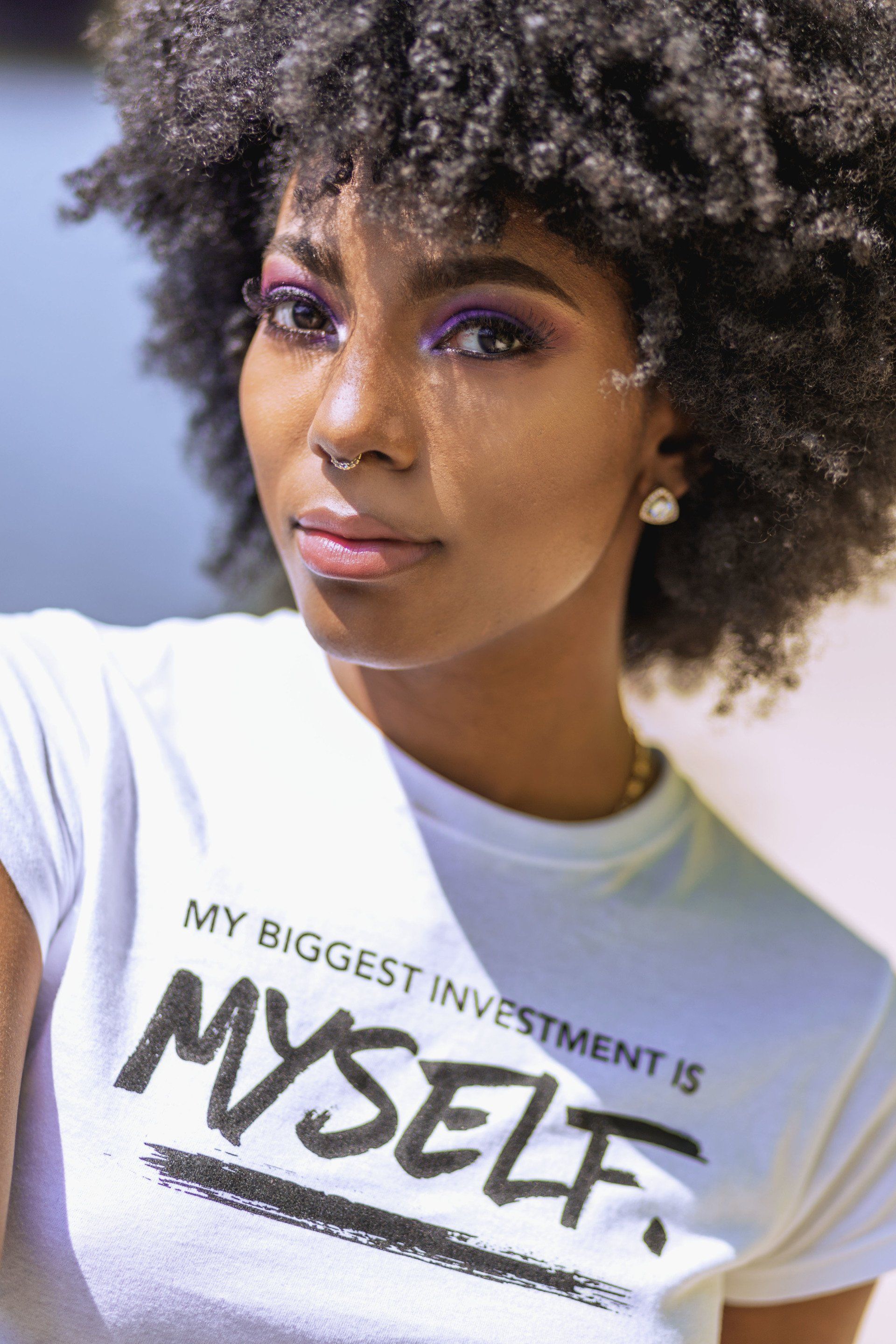 A woman with an afro is wearing a white t-shirt that says `` my biggest investment is myself ''.