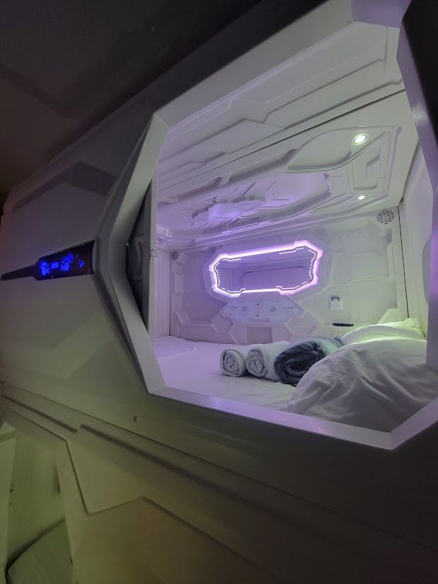 Futuristic capsule hotel room with purple neon lights and bedding.
