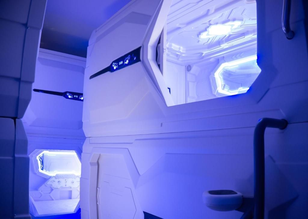 Capsule hotel corridor with bright blue lighting and white sleeping pods.