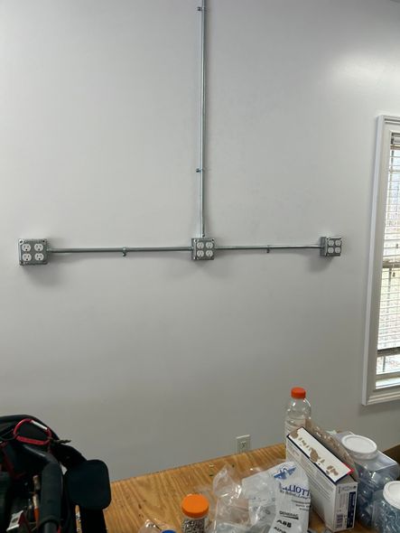 White wall with exposed conduit and electrical boxes above a wooden table with supplies.