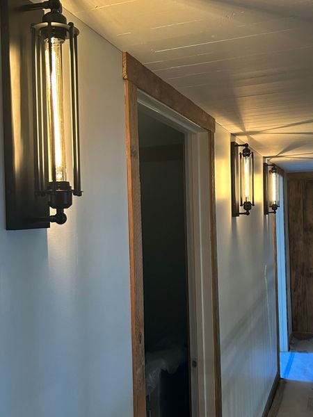 Dim hallway with wall-mounted lantern lights and open doorways, lit by warm indoor light.