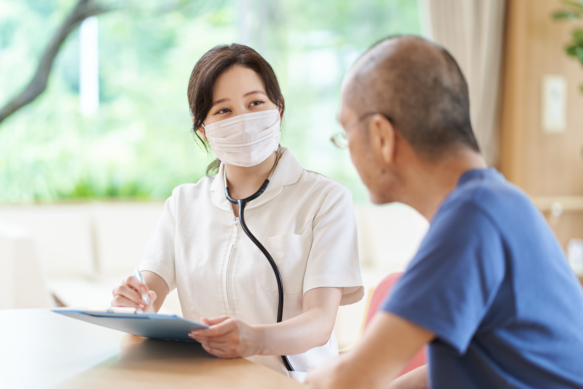 A nurse wearing a mask is talking to an elderly man.