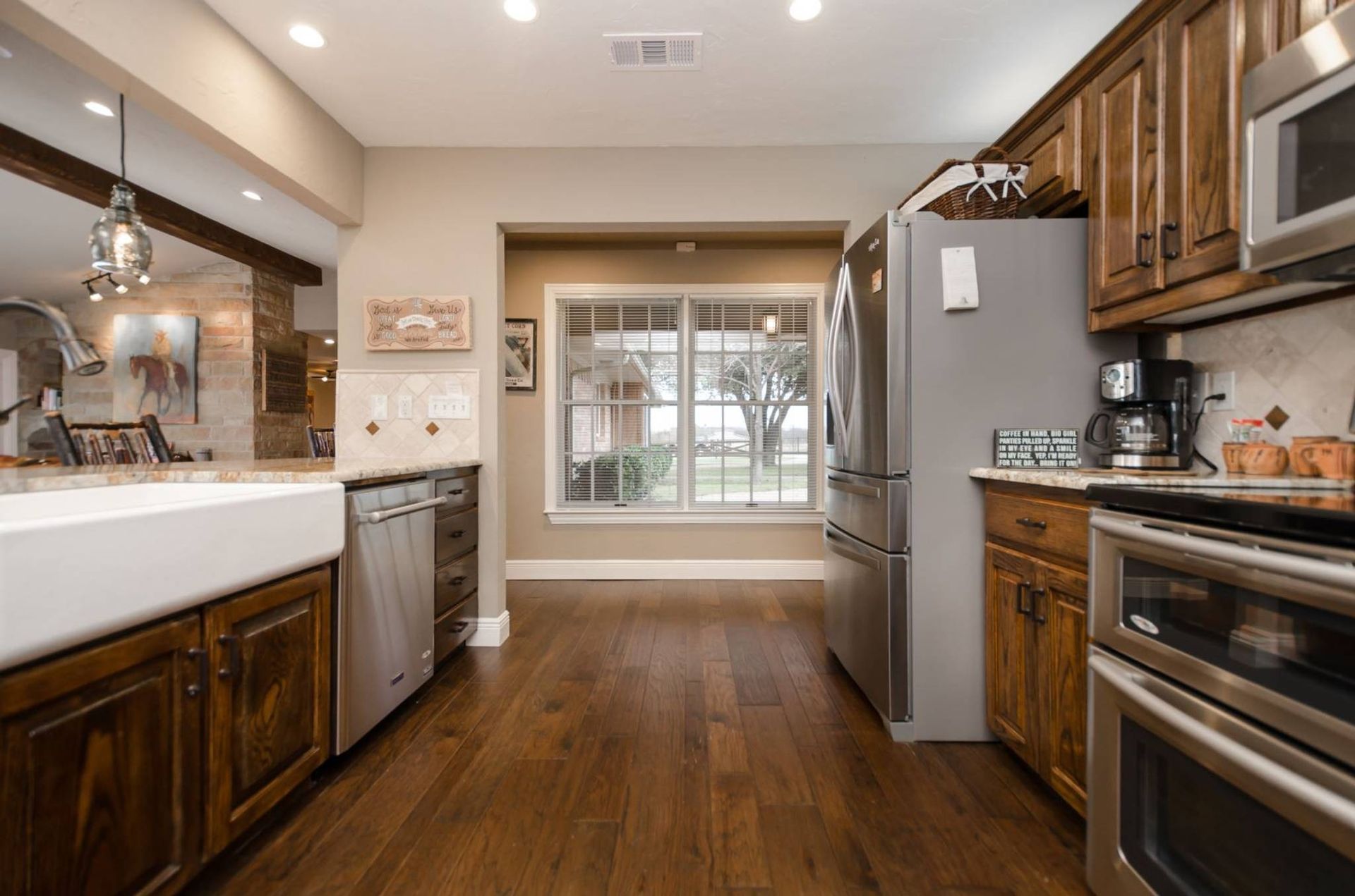 A kitchen with wooden cabinets , stainless steel appliances , and a large window.