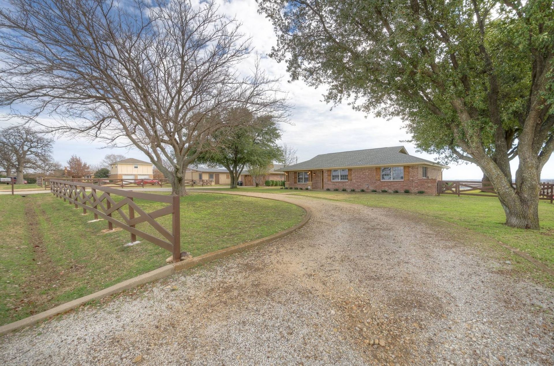 A gravel driveway leading to a brick house with a wooden fence