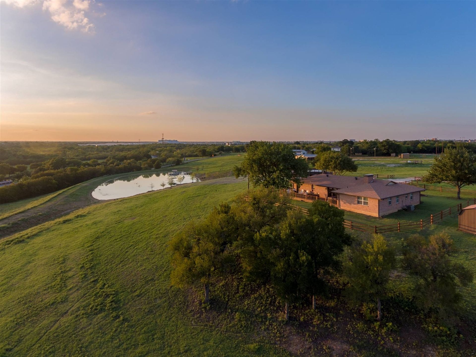 An aerial view of a house sitting on top of a grassy hill next to a pond.