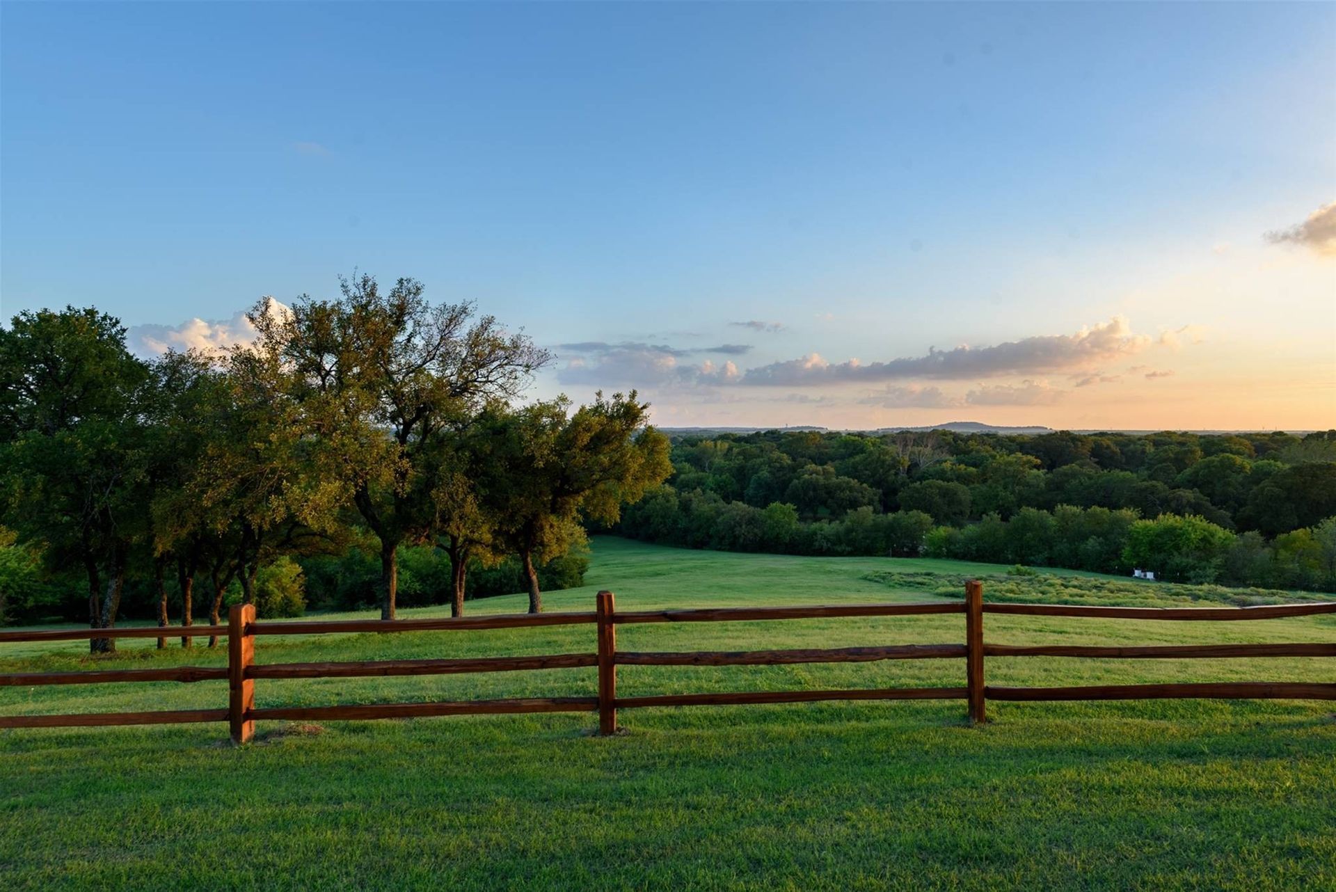 A wooden fence surrounds a grassy field with trees in the background.