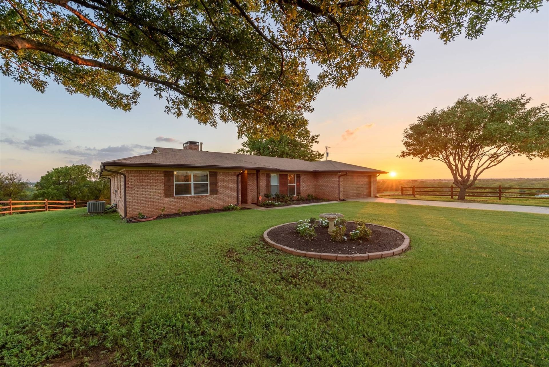 A brick house is sitting in the middle of a lush green field.