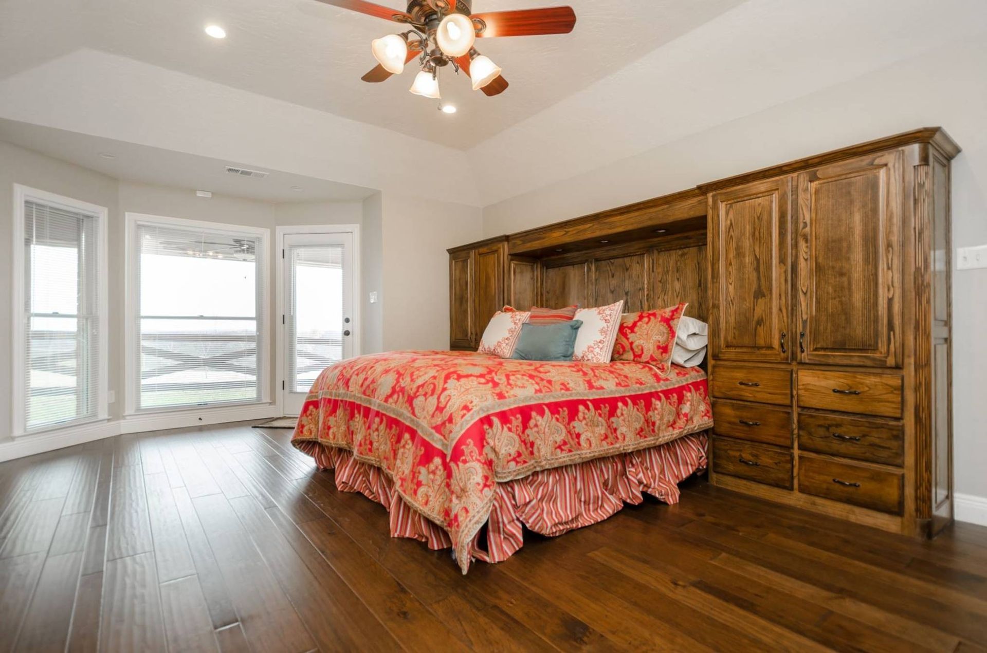 A bedroom with hardwood floors , a bed , a ceiling fan and a large window.