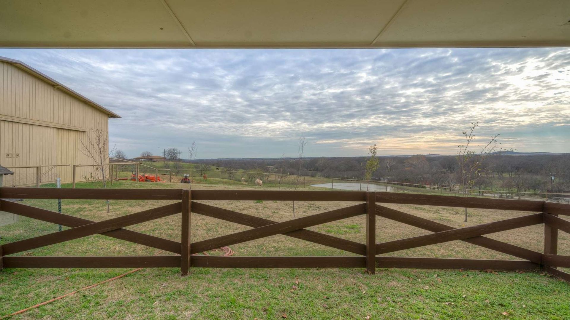 A wooden fence surrounds a grassy field with a barn in the background.