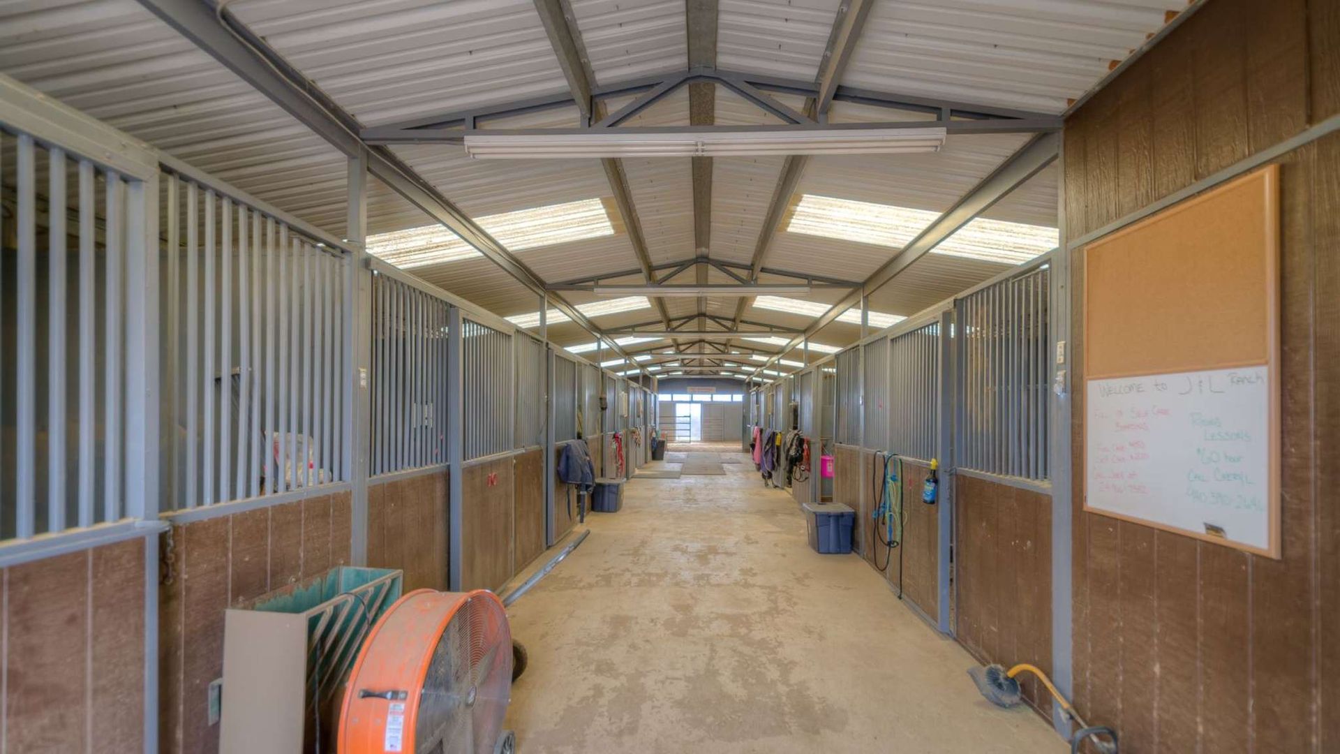 A long hallway in a horse stable with a fan on the floor.
