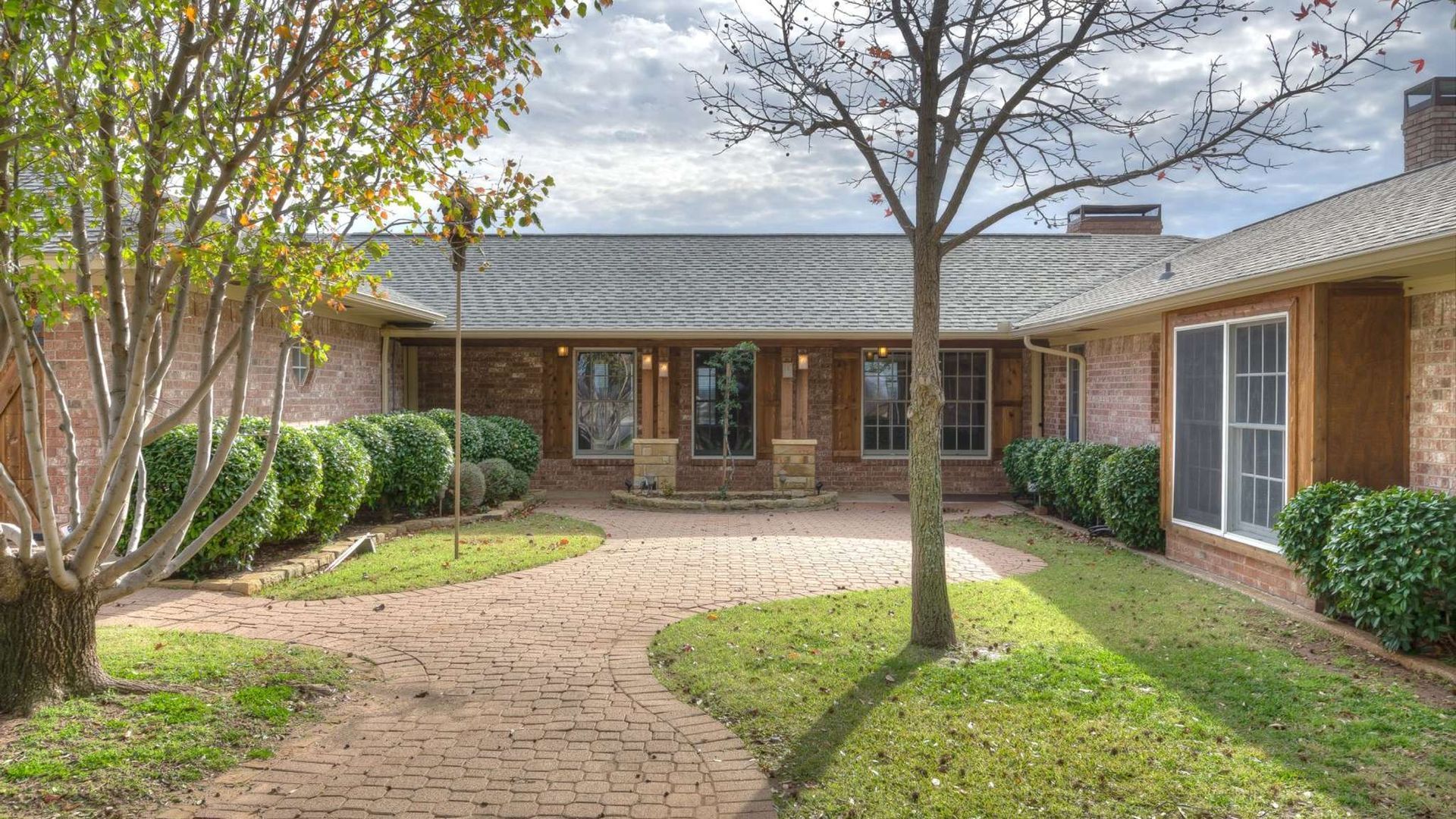 A large brick house with a brick driveway and a tree in front of it.