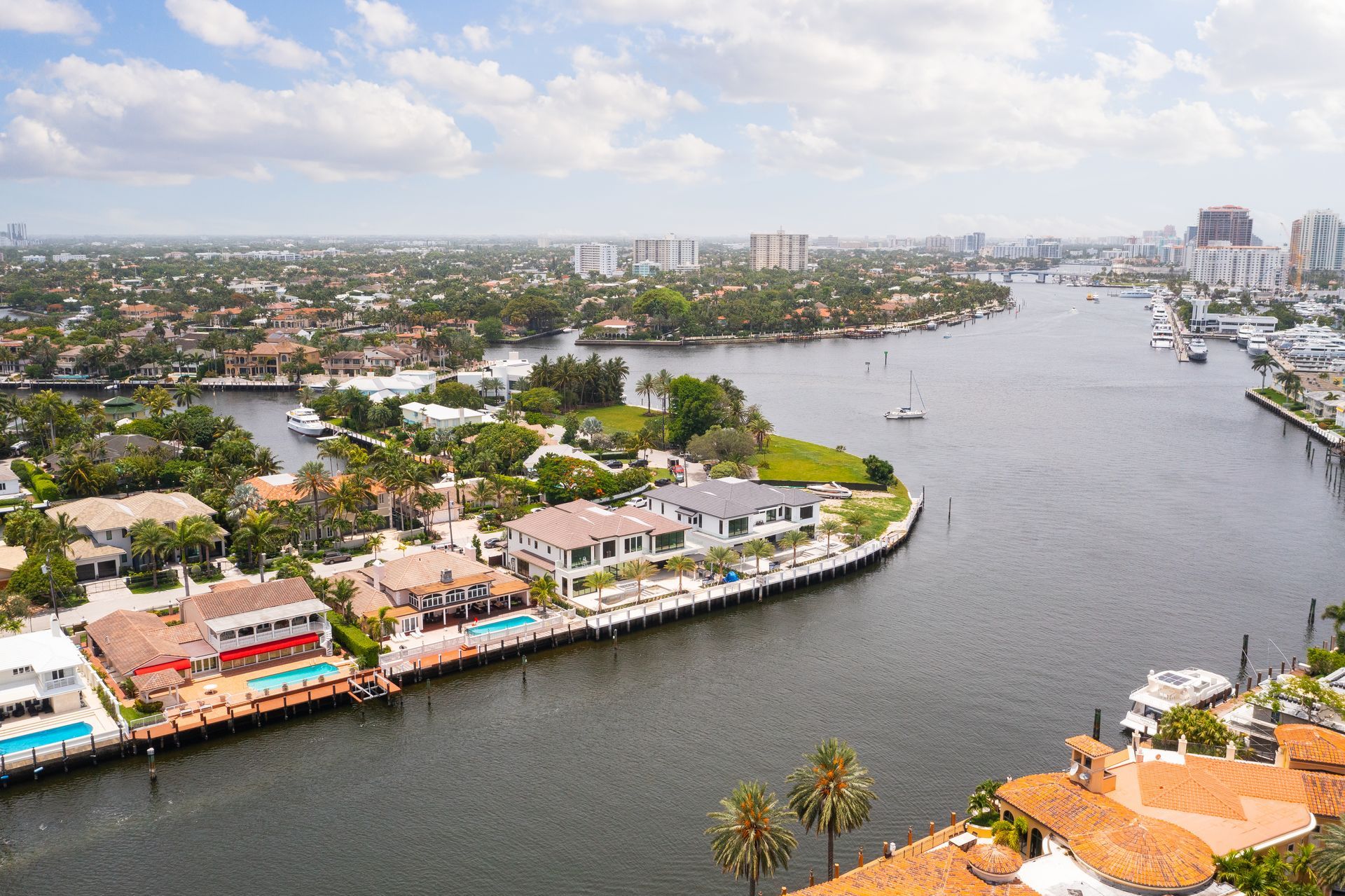 Aerial view of luxury waterfront homes along a waterway in a sunny city.