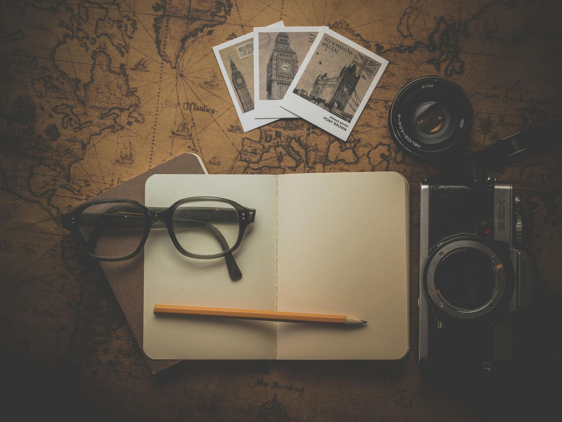 Open notebook with pencil, glasses, camera, and travel photos on a map.