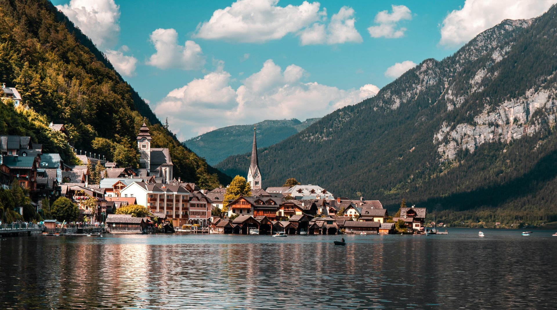 Lakeside village nestled between mountains under a blue sky; wooden houses, church spire.