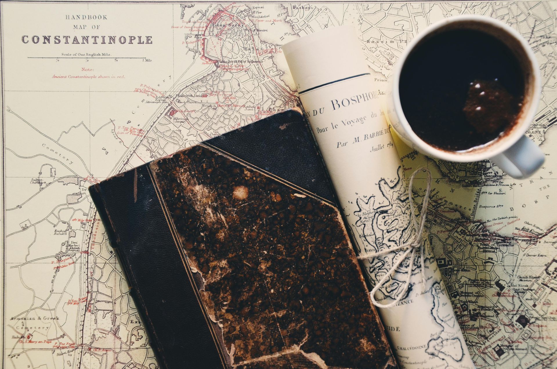 Coffee cup, antique book, and rolled-up map on a vintage map of Constantinople.