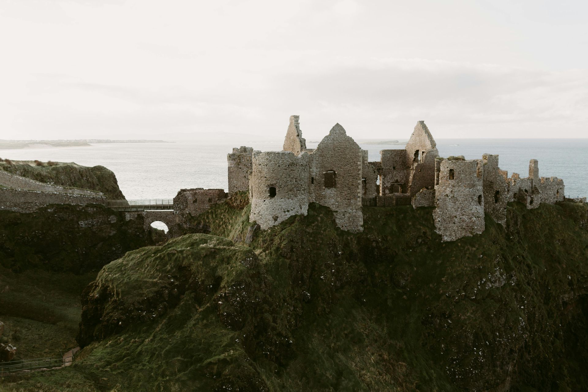 Ruined stone castle on a cliff overlooking the ocean under a cloudy sky.
