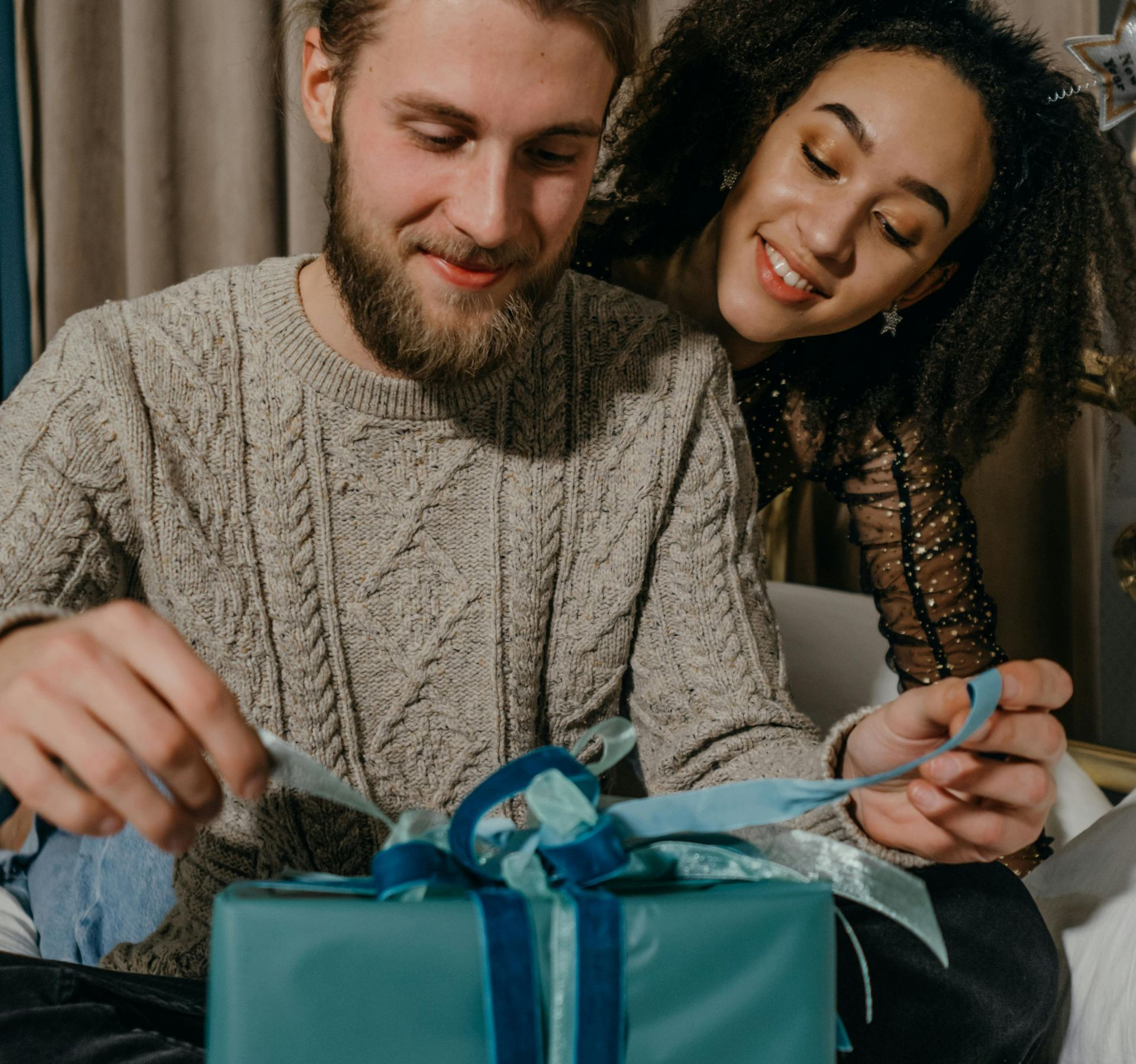 Man unwrapping a gift, woman smiling and watching as she gives the gift of travel.