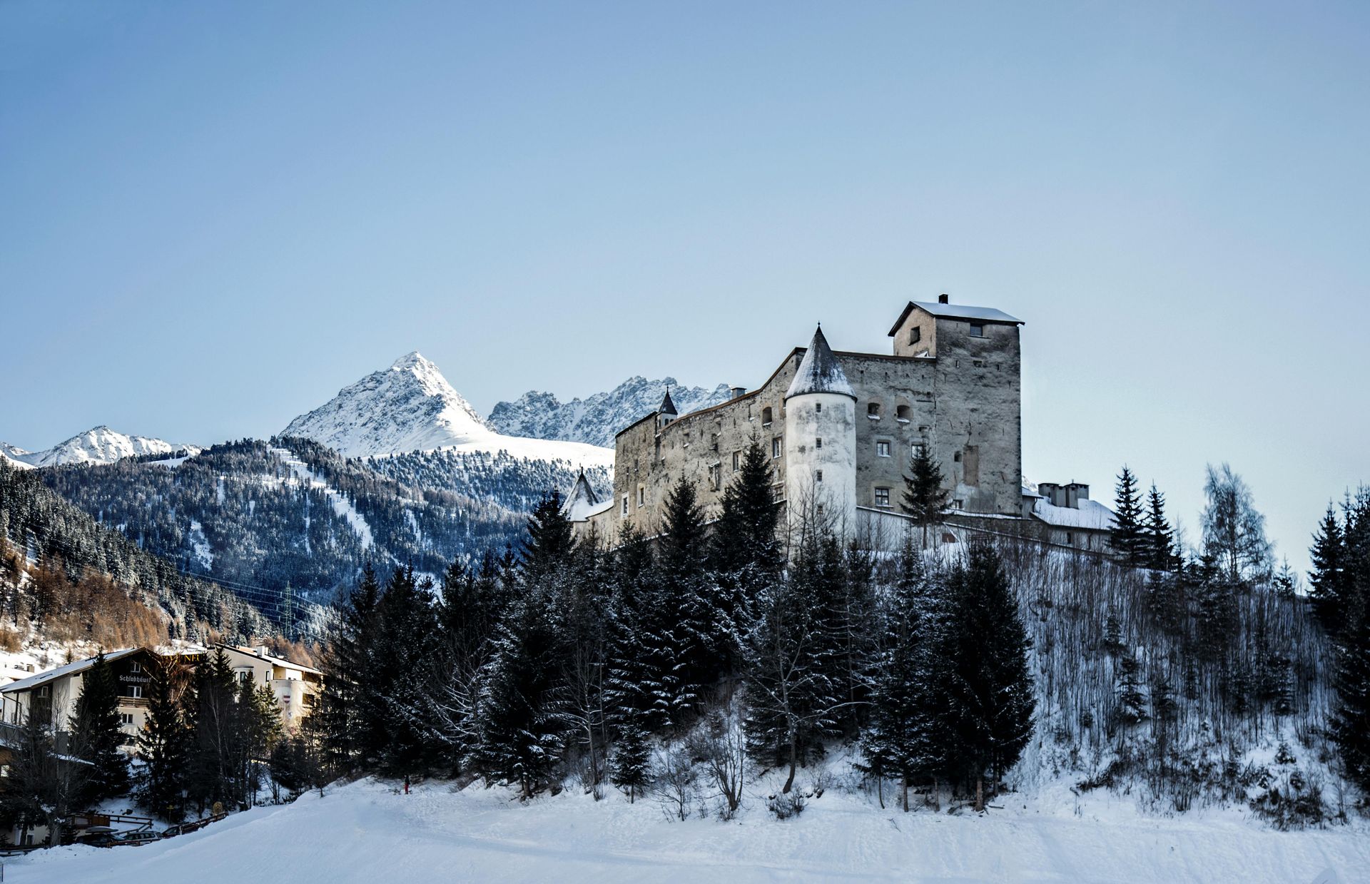 Stone castle on snow-covered hill in a winter landscape; mountains and trees in background. Ideal present for a Holiday Trip