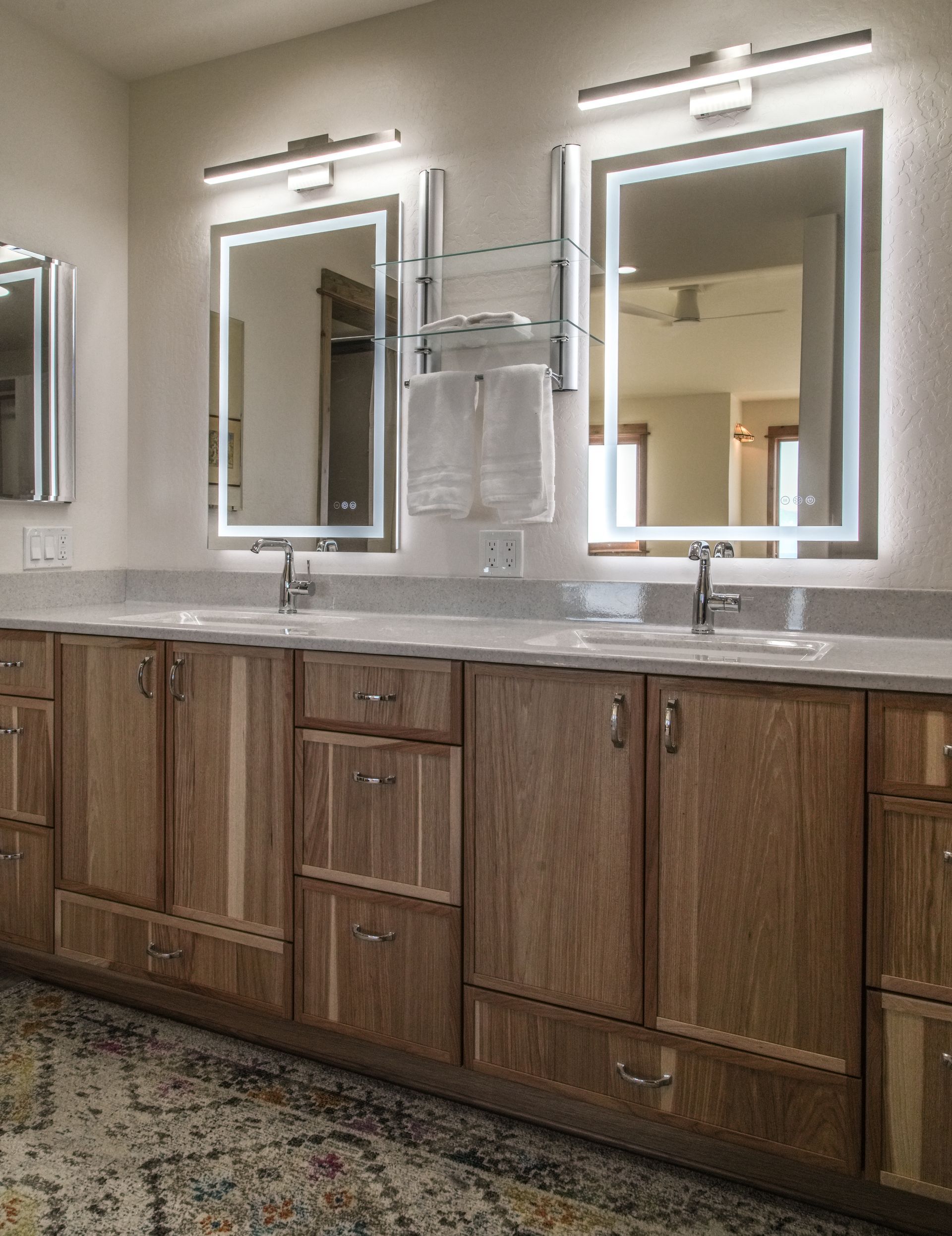 Bathroom with two sinks, large mirrors with LED lighting, and light wood cabinetry.