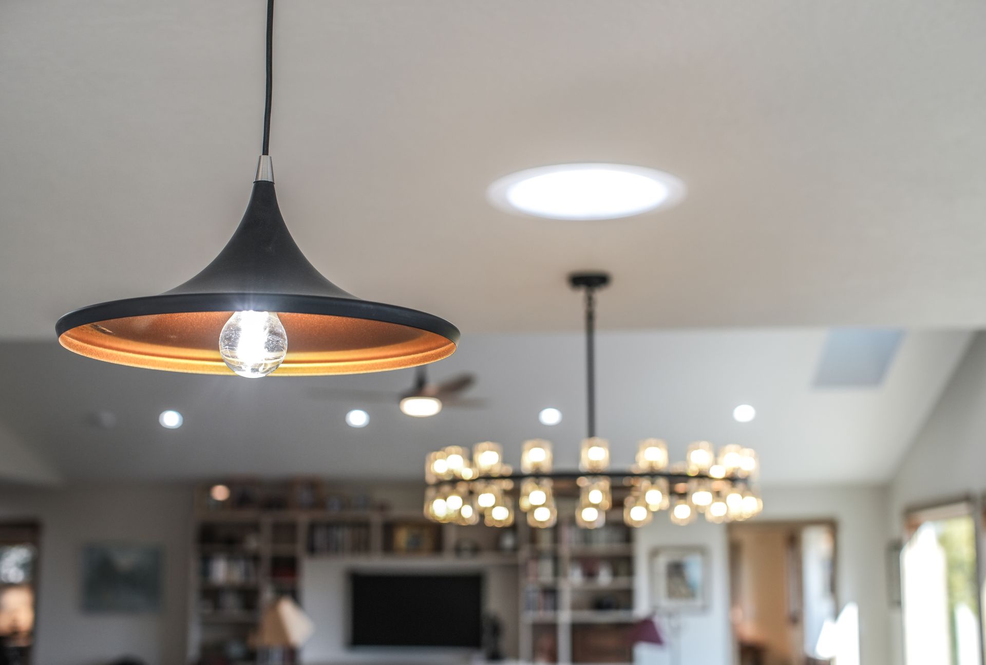 Black pendant lamp and chandelier in a room with a skylight.