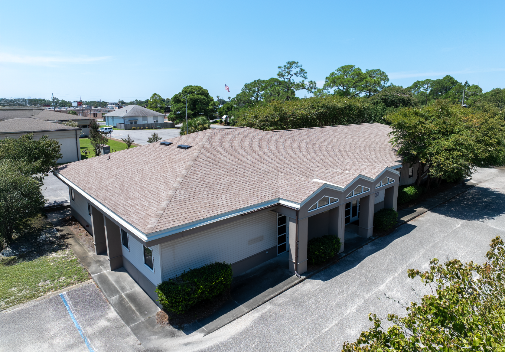 Low-angle view of a light brown, one-story building with dark roof and several columns. Surrounded by trees and blue sky.
