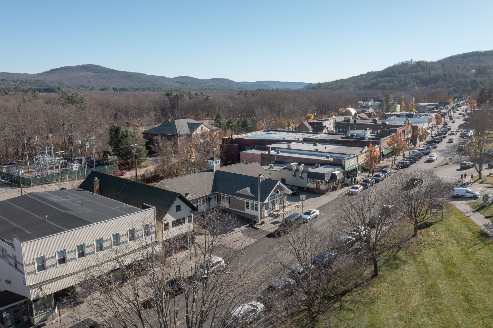 An aerial view of a small town with buildings along a street and a mountain backdrop.