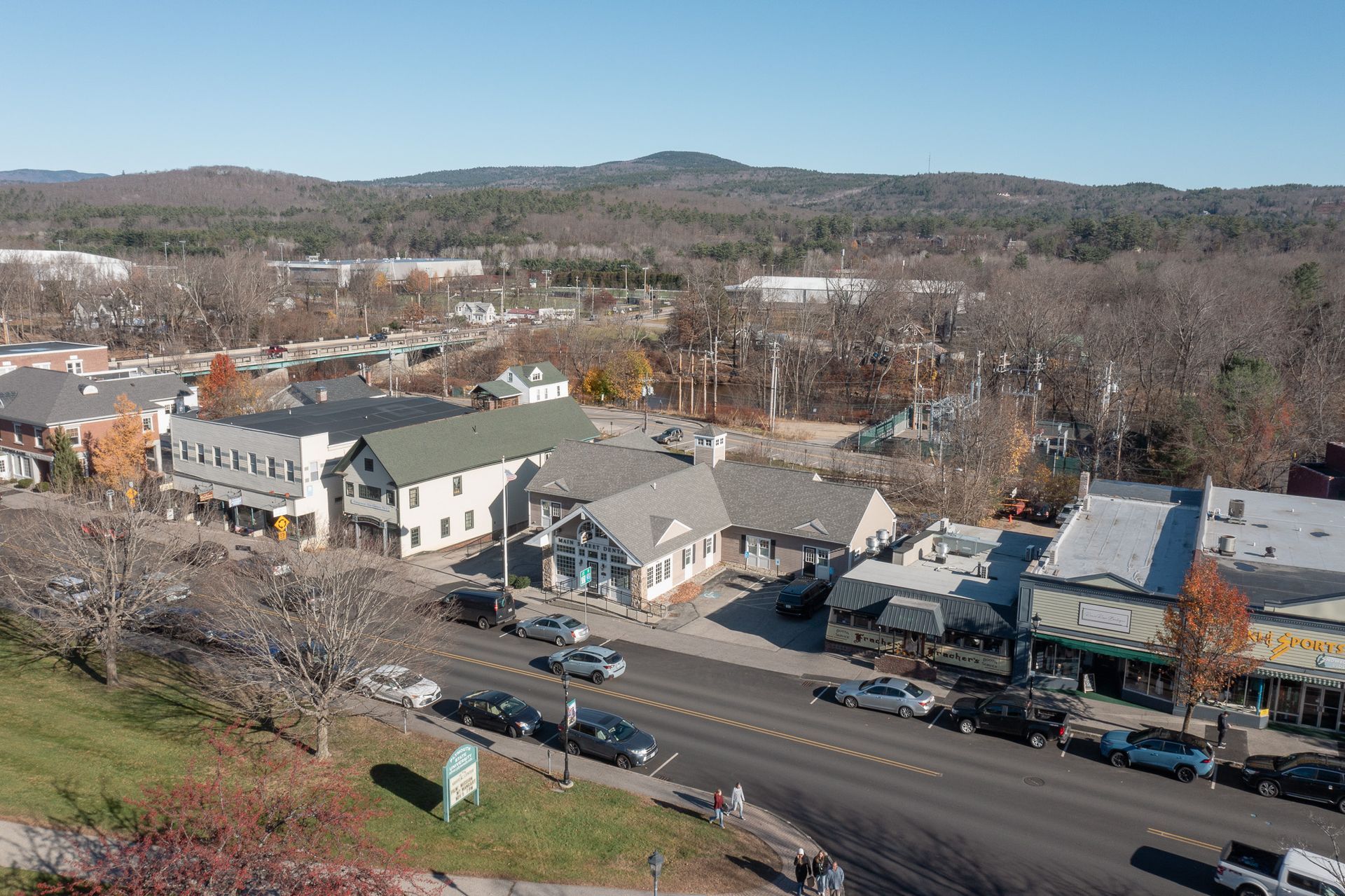 Aerial view of a street in a town; buildings, trees, cars, and mountains in the distance.