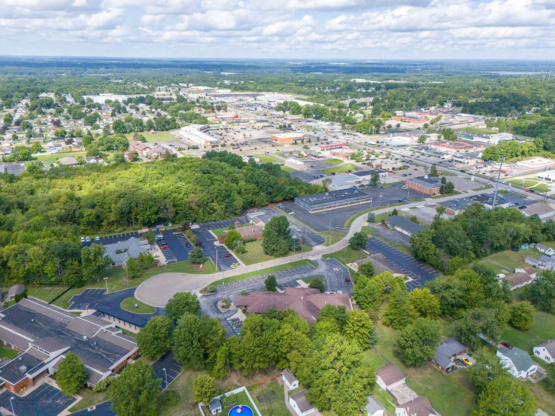 Aerial view of a town with buildings, trees, and roads under a cloudy sky.