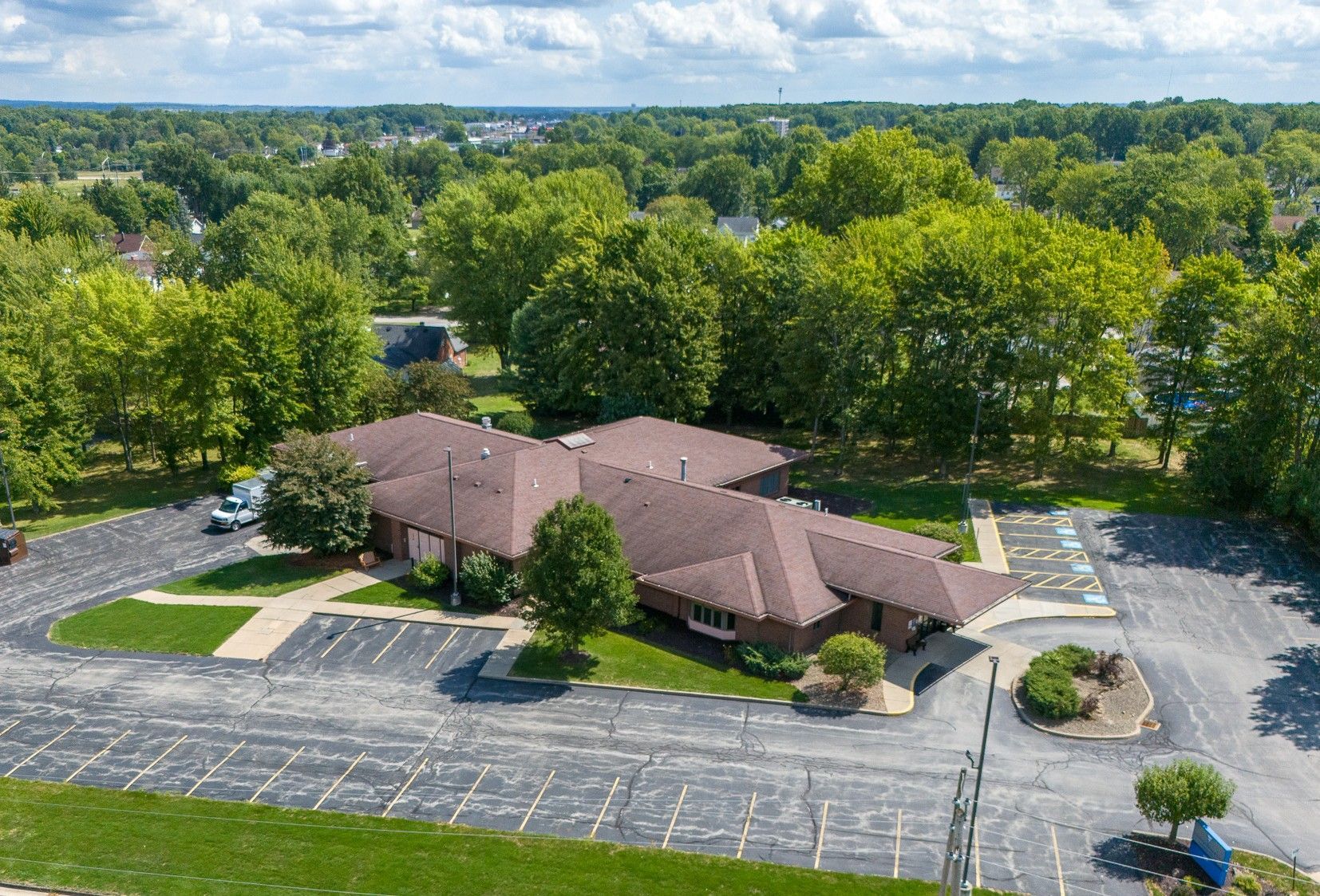 Fresenius medical care dialysis center in austintown ohio with a curved roof surrounded by lush green trees and a parking lot on a sunny day.