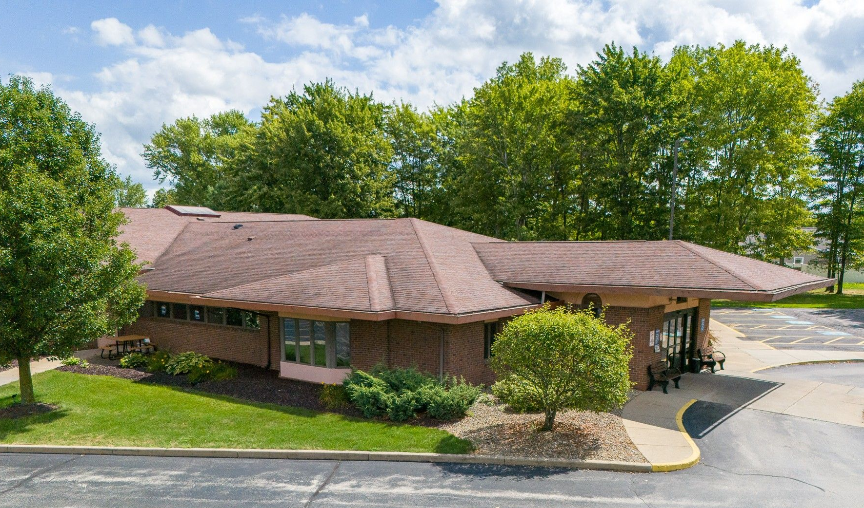 Low-rise dialysis building with brown roof, green lawn, and trees under a blue sky.