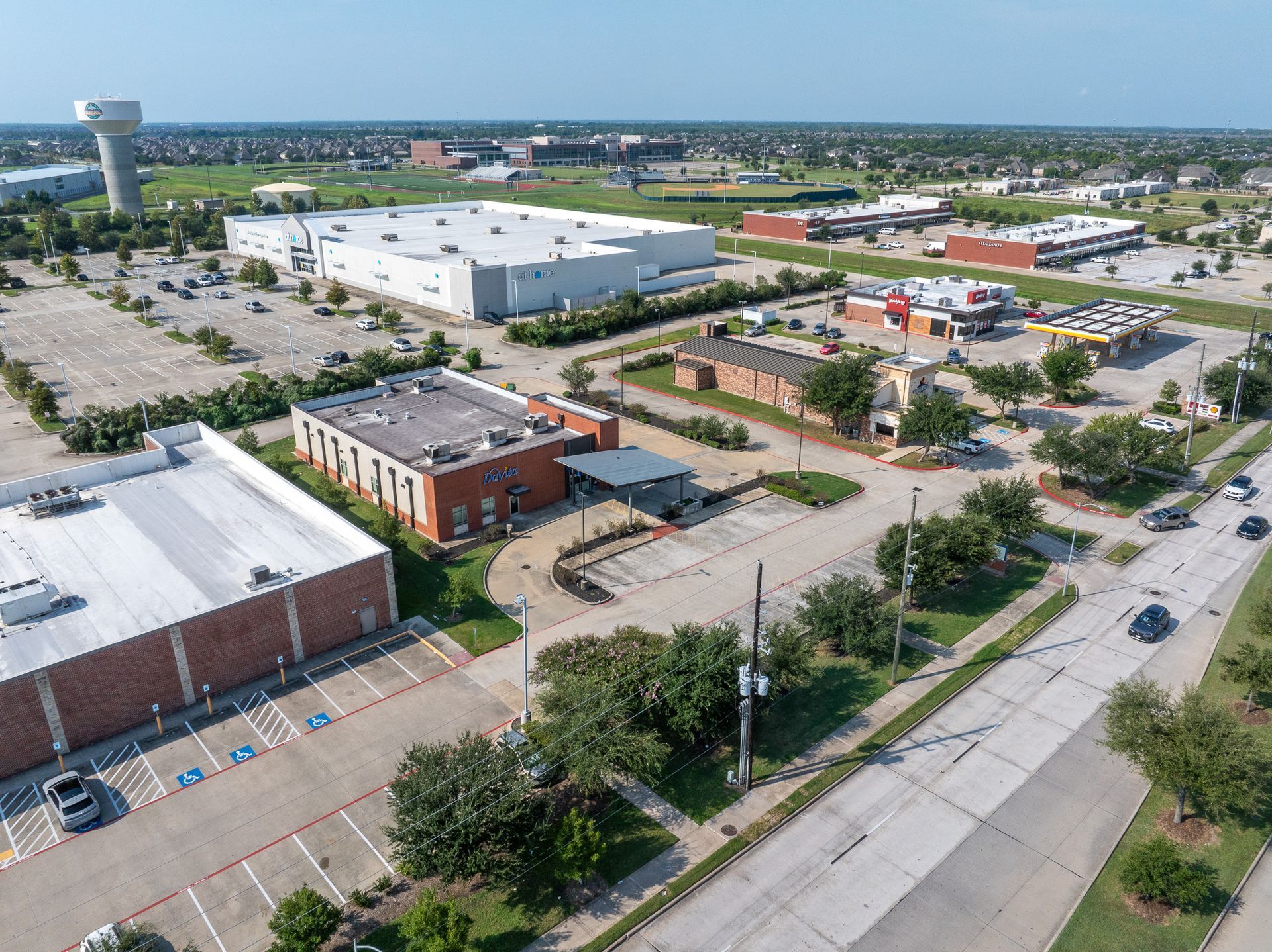 Aerial view of buildings, parking lots, and a road in a suburban setting; sunny day.