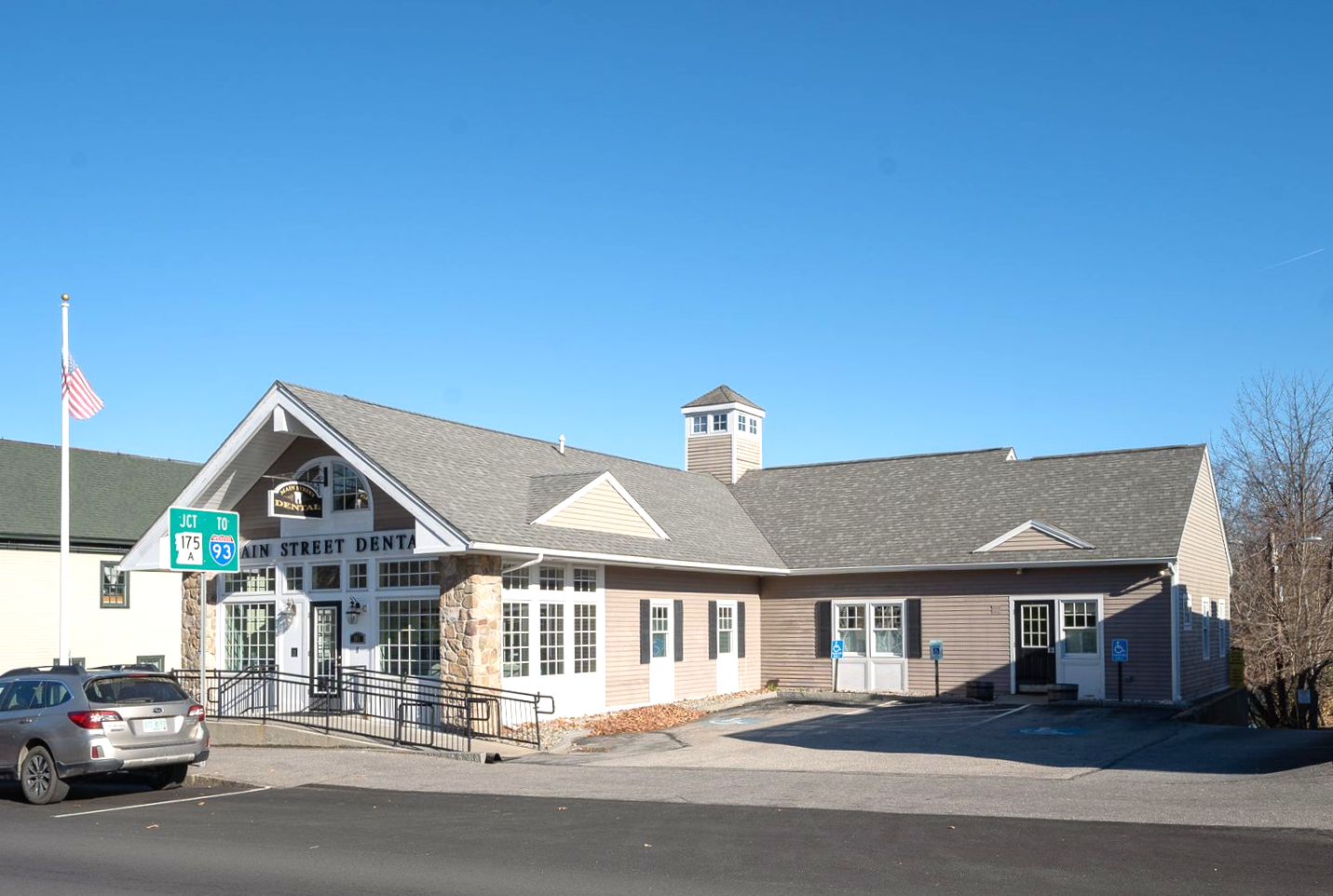 Exterior view of a Heartland Dental, an American flag, and parked cars on a sunny day.