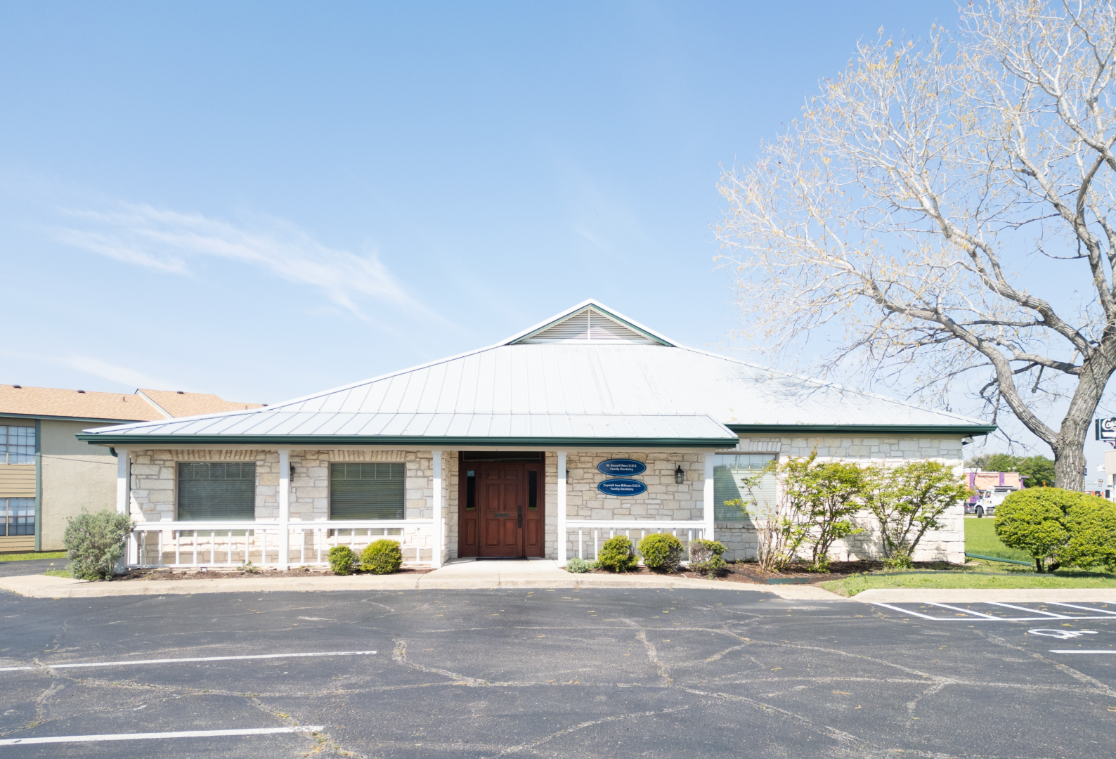 A white heartland dental office with a green roof and a parking lot in front of it.