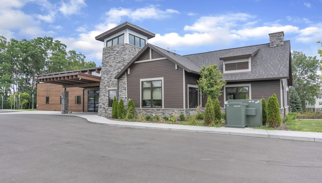 Brown and stone building with a tower and covered entrance, set against a blue sky with trees.