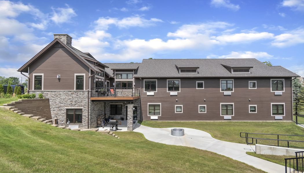 A brown two-story building with stone accents, a sloping lawn, and a partly cloudy sky.